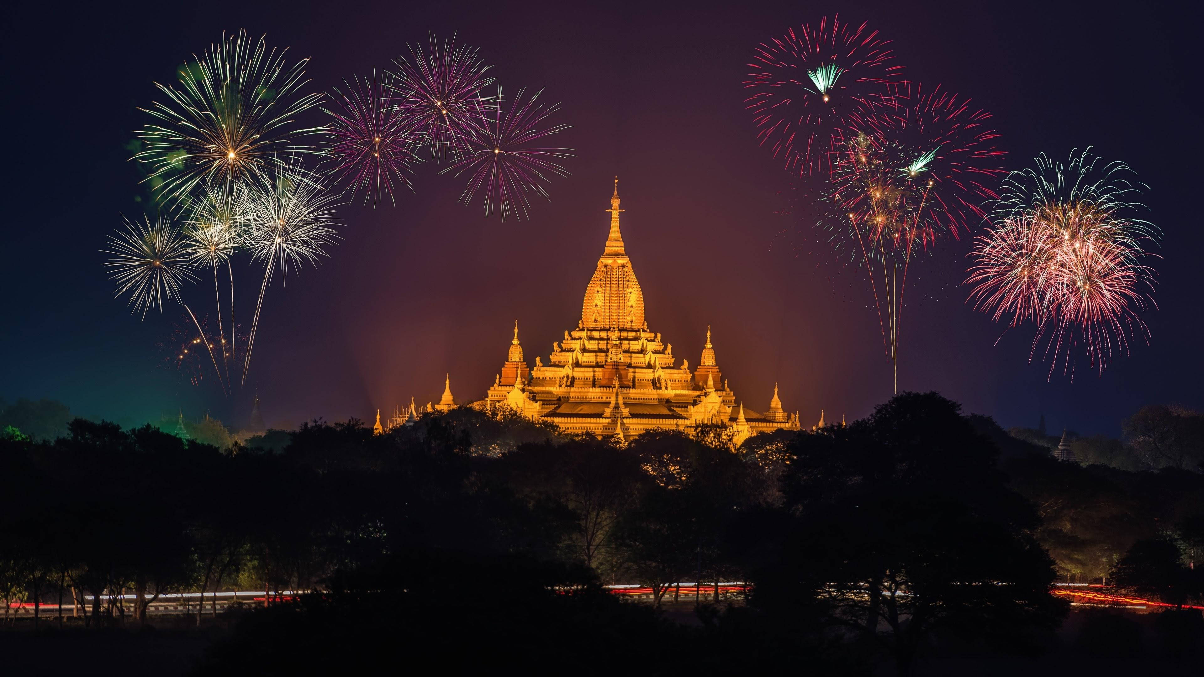 Burma 桌布 壁紙 — 一座宏偉的金色寶塔在夜晚被照亮，周圍是黑暗天空中綻放的鮮豔煙火。