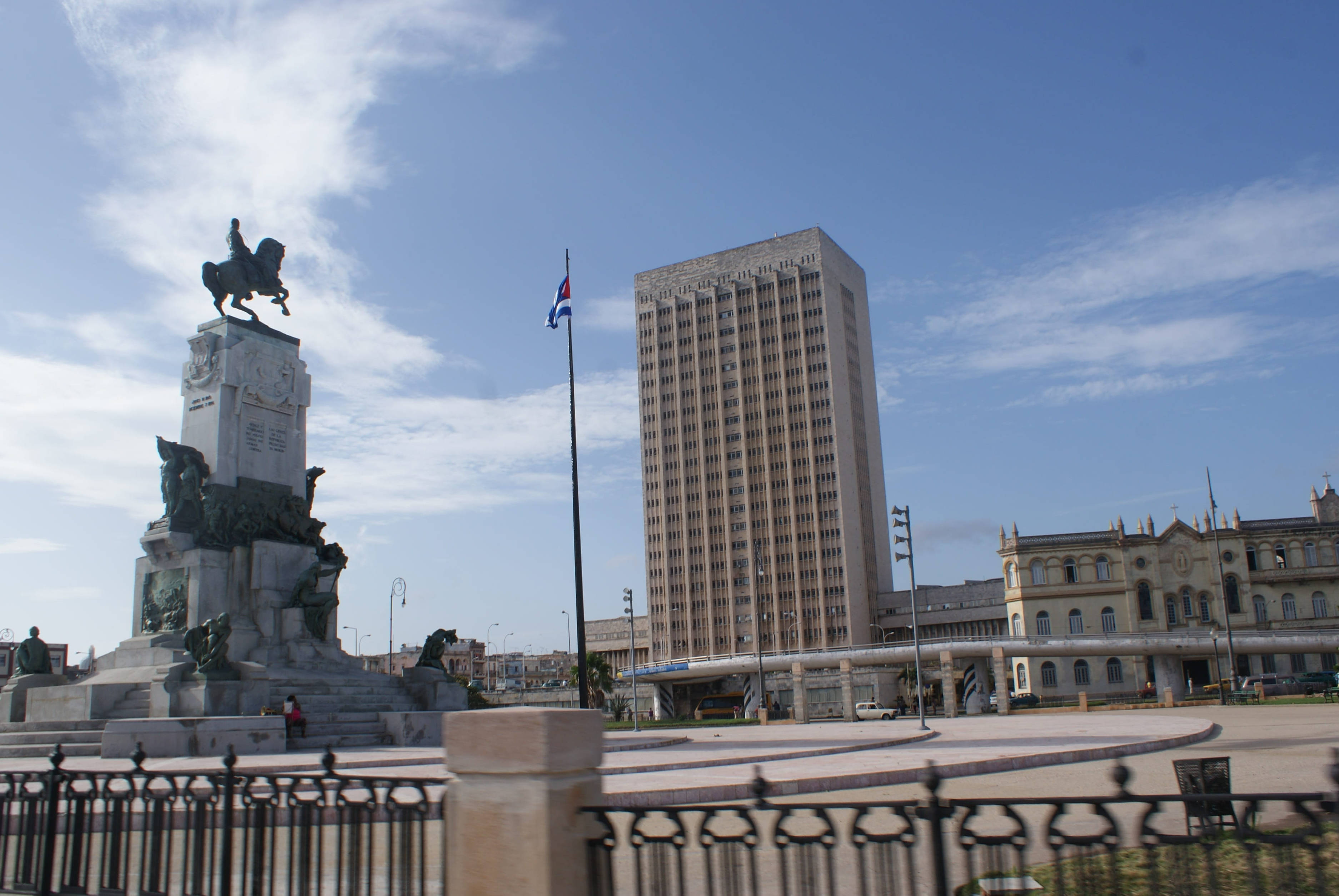 Cuban 桌布 壁紙 — 一座宏偉的騎馬雕像矗立在陽光普照的廣場上，旁邊是高聳的現代建築和歷史建築，藍天白雲。