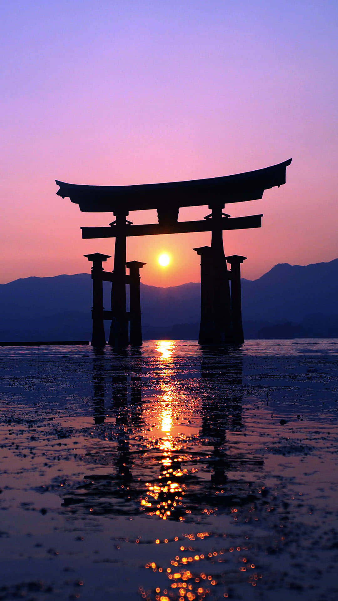 日本 桌布 壁紙 — 一座宏偉的鳥居在暮色水中呈現剪影，夕陽在遠山後落下，投下金色倒影。