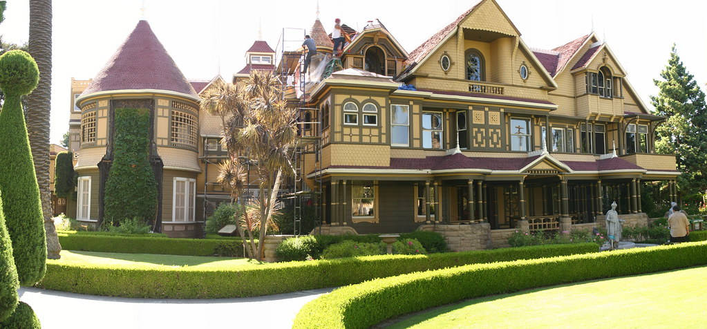 Mansion 桌布 壁紙 — 一座宏偉的黃色維多利亞式豪宅，擁有紅色屋頂和修剪整齊的樹籬，在明亮的日光下。
