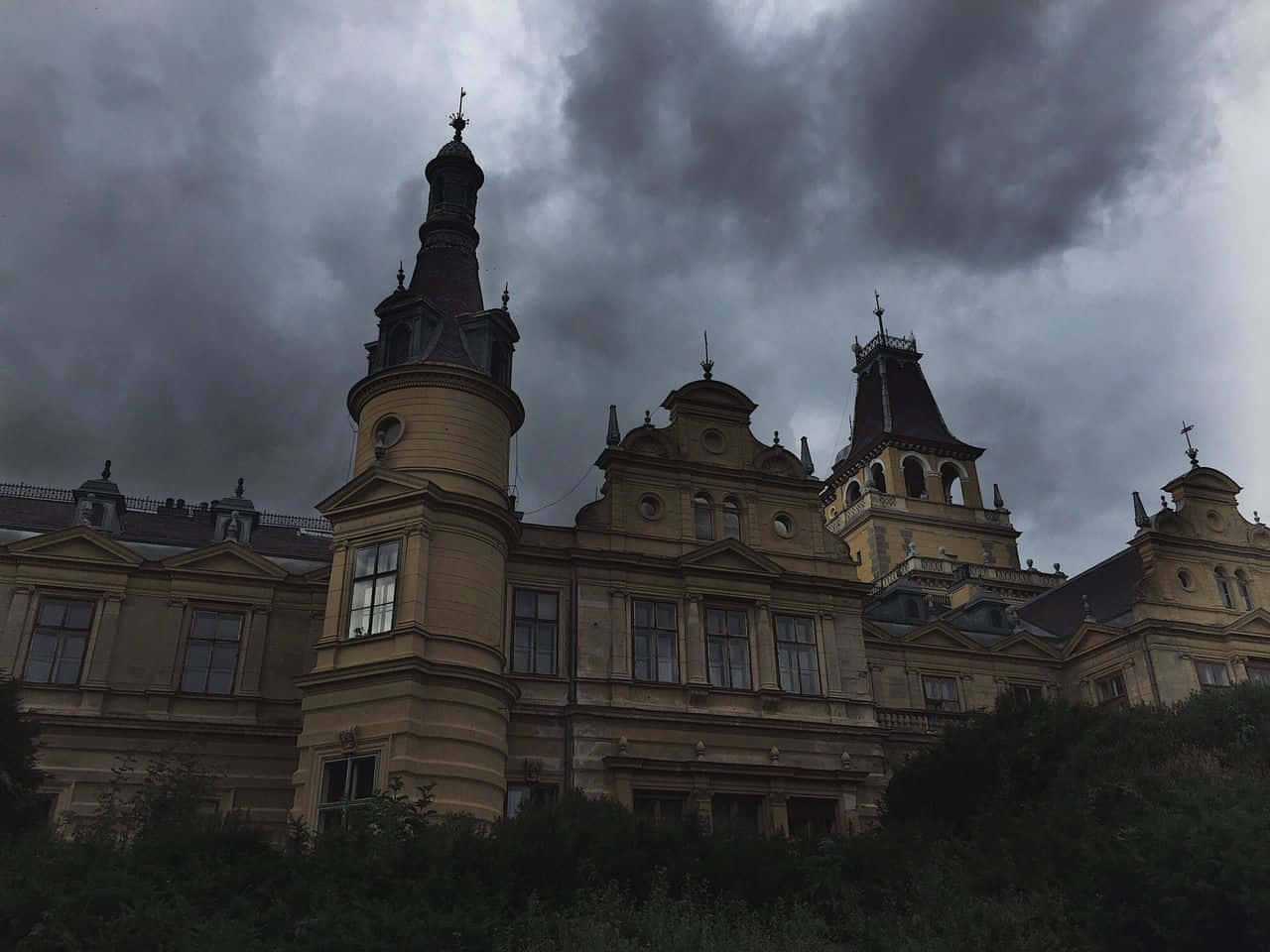 Dark Academia Aesthetic 桌布 壁紙 — 一座宏偉華麗的城堡，帶有塔樓和圓頂，在沉重、暴風雨的灰色天空下若隱若現。