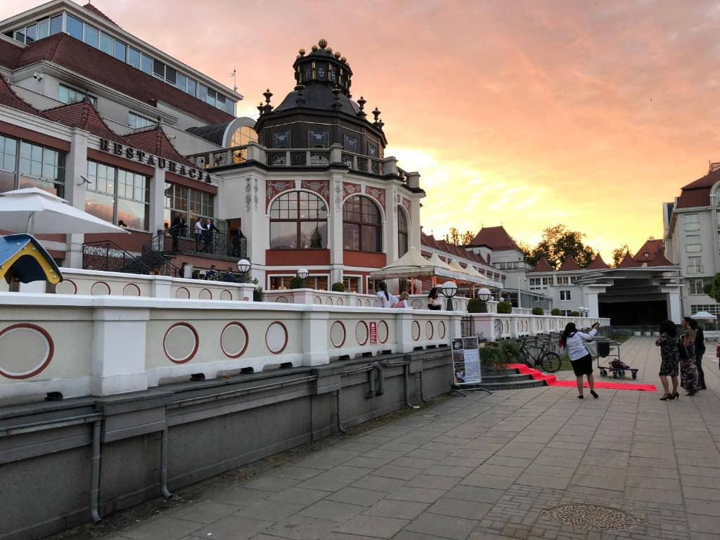 高清 桌布 壁紙 — 一座宏偉華麗的建築，紅頂白牆，在夕陽下矗立，溫暖的陽光灑在鋪砌的行人道上，人們在那裡漫步和戶外用餐。
