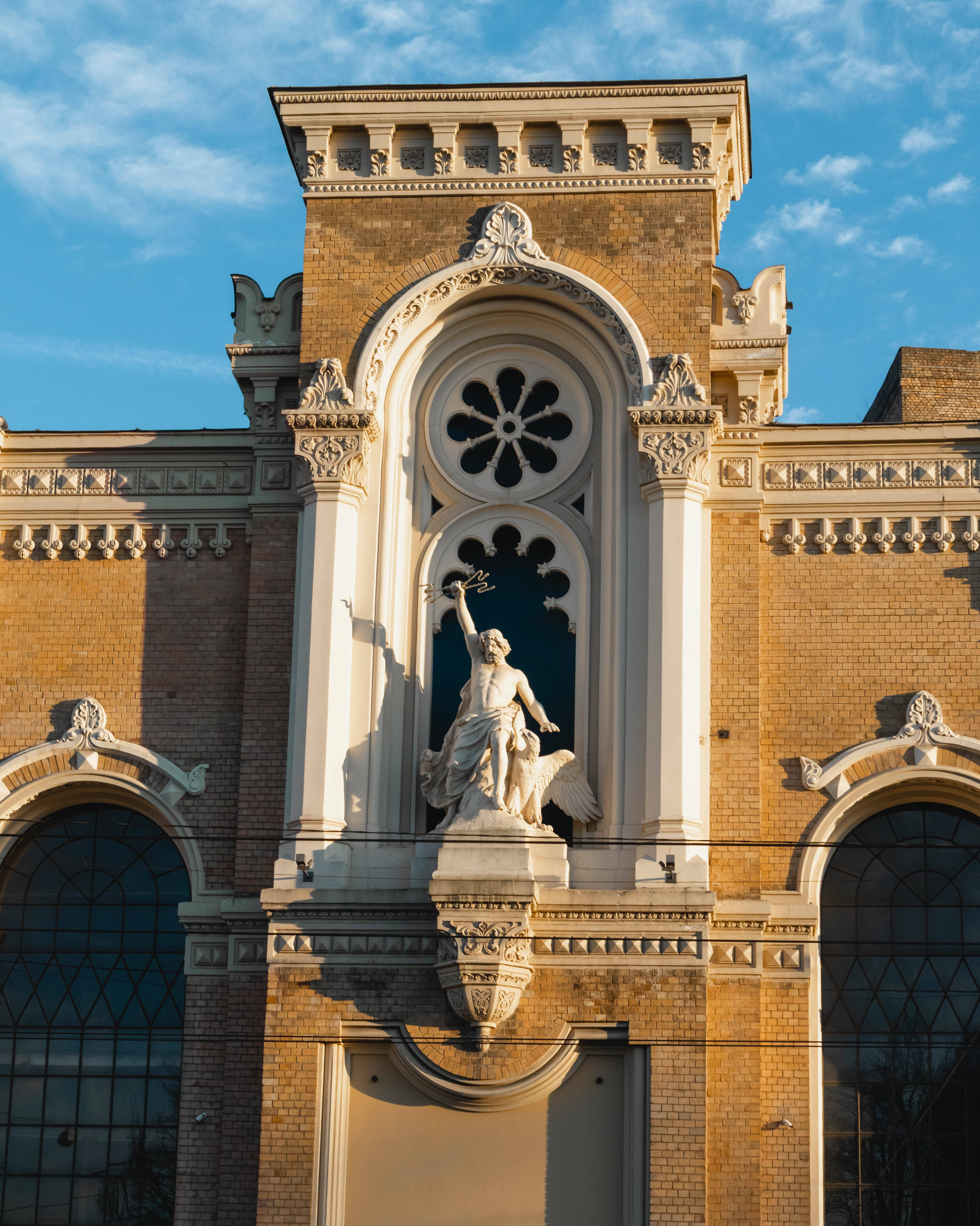 Latvia 桌布 壁紙 — 一座宏偉華麗的建築外牆，中央有一座帶翼人物雕像，手持桂冠，背景是藍天。