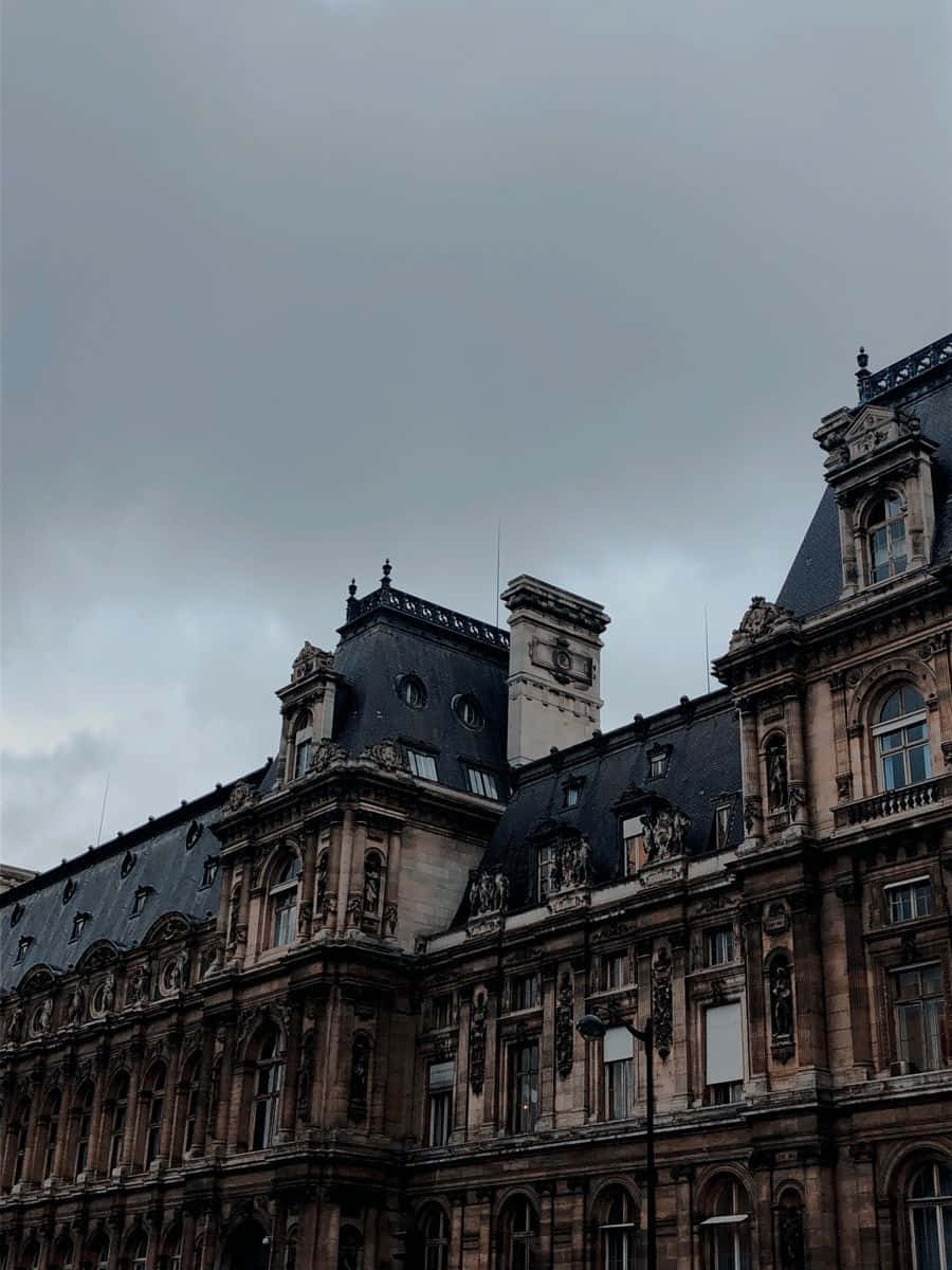 Dark Academia Aesthetic 桌布 壁紙 — 一座宏偉華麗的石建築，擁有深色石板屋頂和精緻雕刻，在沉重的灰色天空下。