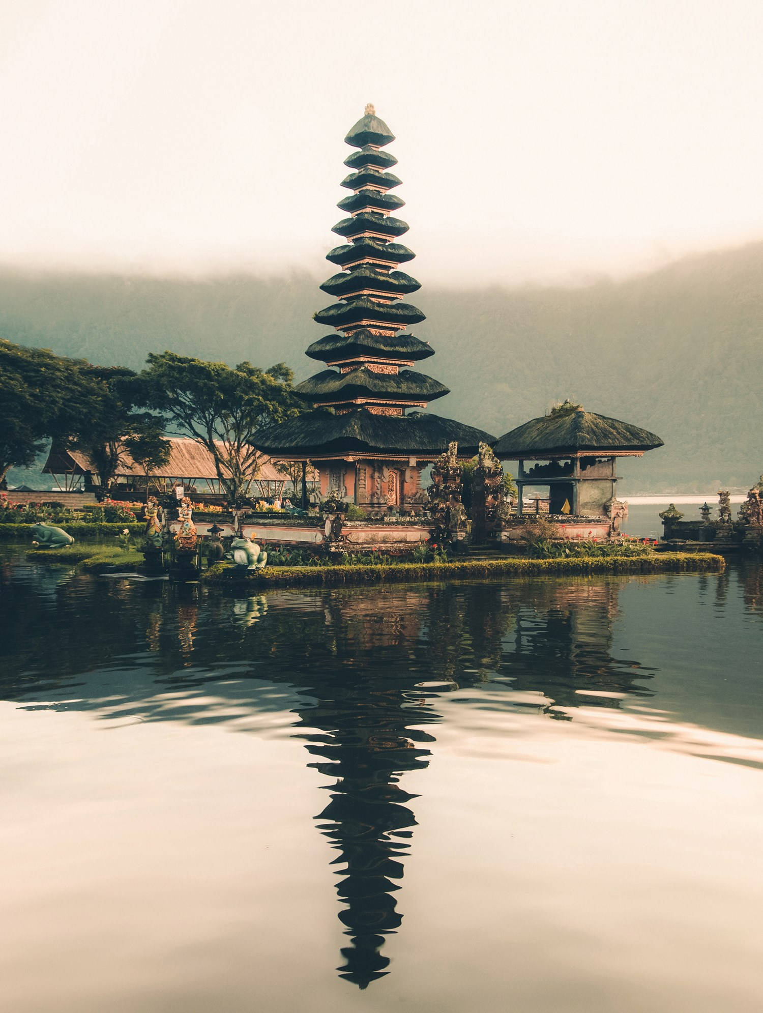 Vacation 桌布 壁紙 — 一座寧靜的峇里島寺廟，層疊的屋頂完美倒映在平靜的湖水中，四周環繞著霧氣繚繞的山巒。