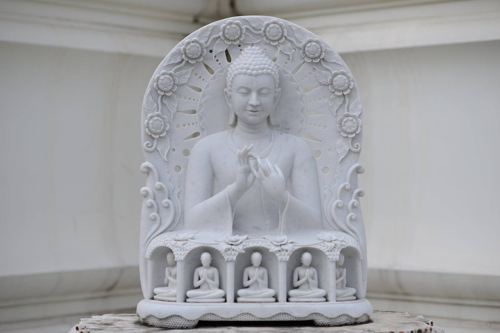 Gautam Buddha 桌布 壁紙 — 一座寧靜的白色大理石佛像，帶有精緻的花卉雕刻，下方有四個較小的坐佛。