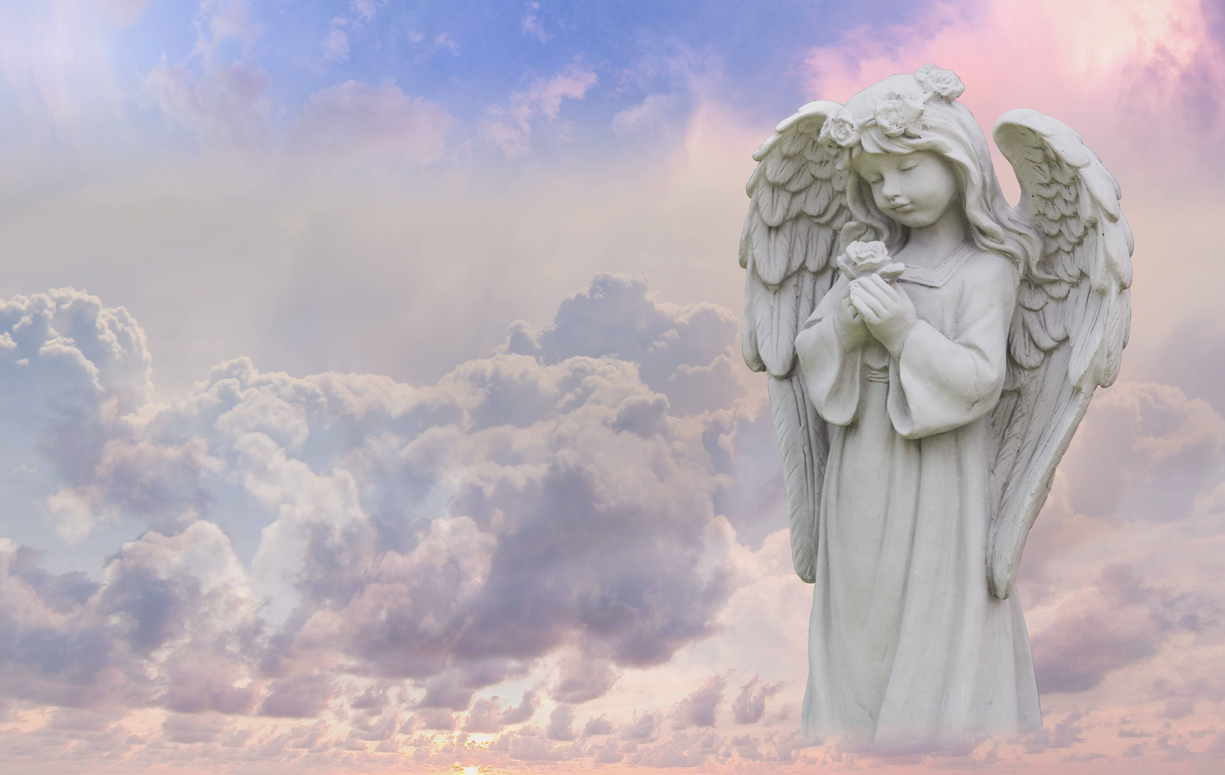 angels 桌布 壁紙 — 一座寧靜的白色天使雕像在日落時分，手持一朵花，映襯著柔和粉彩的天空和蓬鬆的雲朵。