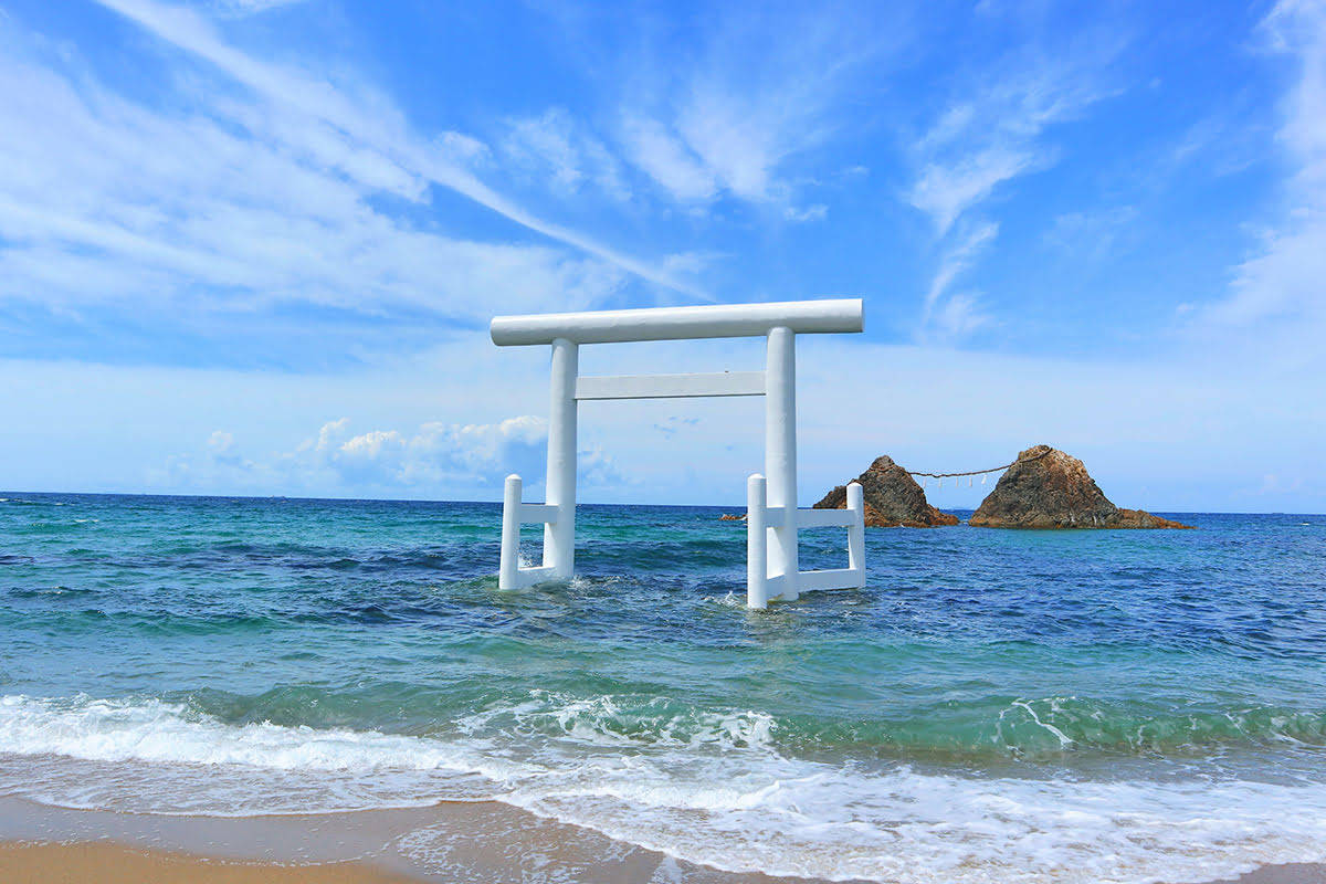 Fukuoka 桌布 壁紙 — 一座寧靜的白色鳥居部分浸沒在碧綠的海水中，上方是晴朗的藍天，點綴著縷縷白雲。