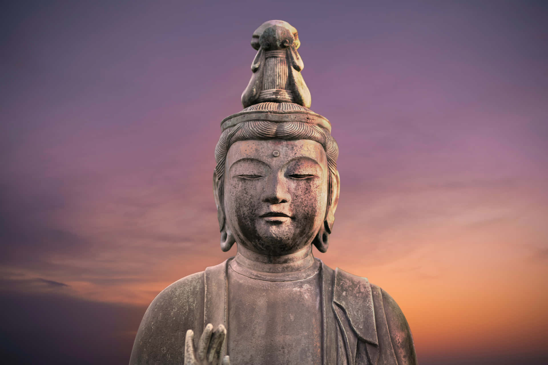 佛陀 桌布 壁紙 — 一座寧靜的石佛像，閉著眼睛，戴著皇冠，背景是紫色和橙色的暮色天空。
