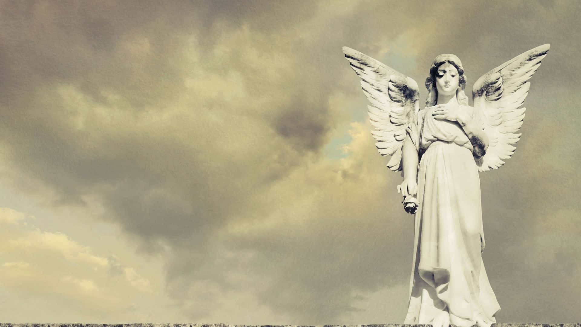 天使 桌布 壁紙 — 一座寧靜的石天使雕像，展開翅膀，矗立在戲劇性的多雲天空下。