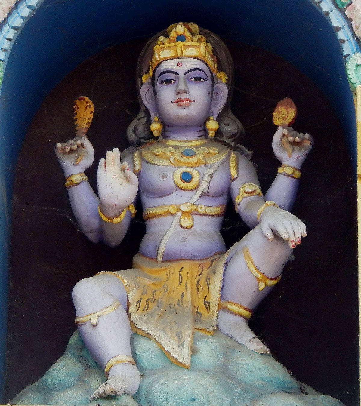 statue 桌布 壁紙 — 一座寧靜的紫色皮膚印度教神像，戴著金色皇冠和珠寶，盤腿坐在壁龕中，手持象徵性物品。