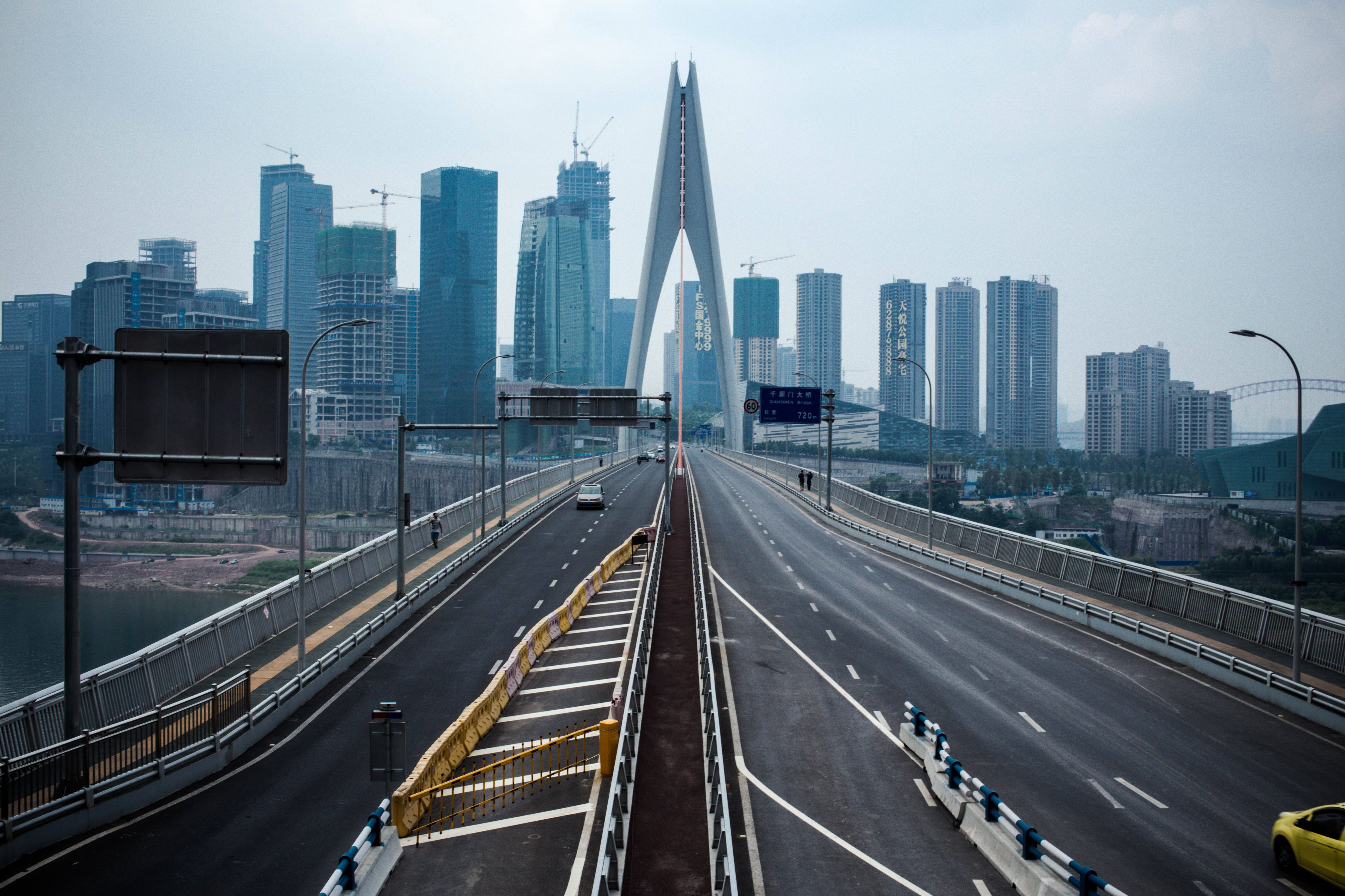 Chongqing 桌布 壁紙 — 一座寬闊的現代橋樑在陰天中延伸向高聳的城市天際線，路上車輛稀少。