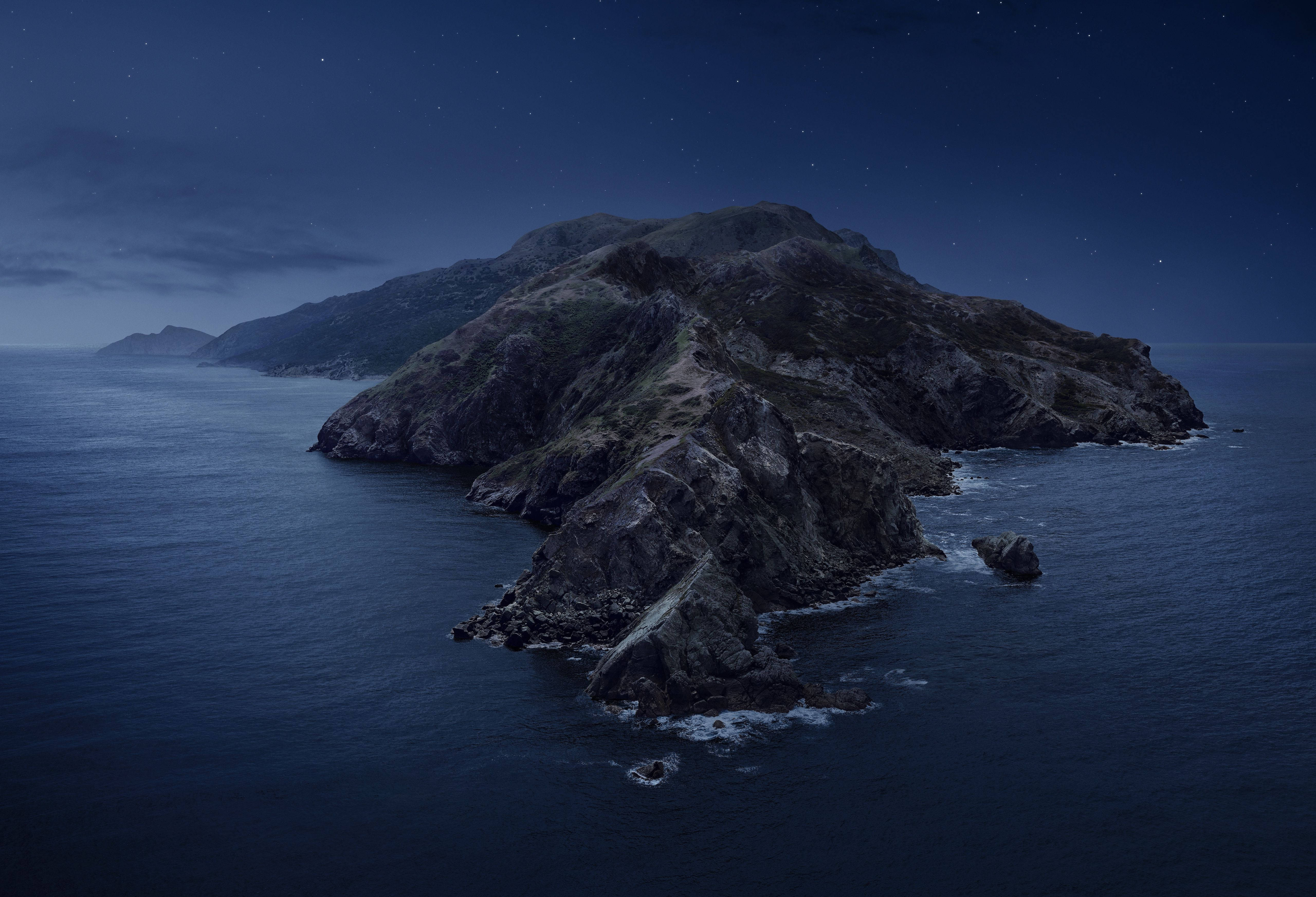 Catalina 桌布 壁紙 — 一座崎嶇的岩石島嶼從深藍色的海洋中升起，在繁星點點的夜空下，溫柔的海浪拍打著懸崖。