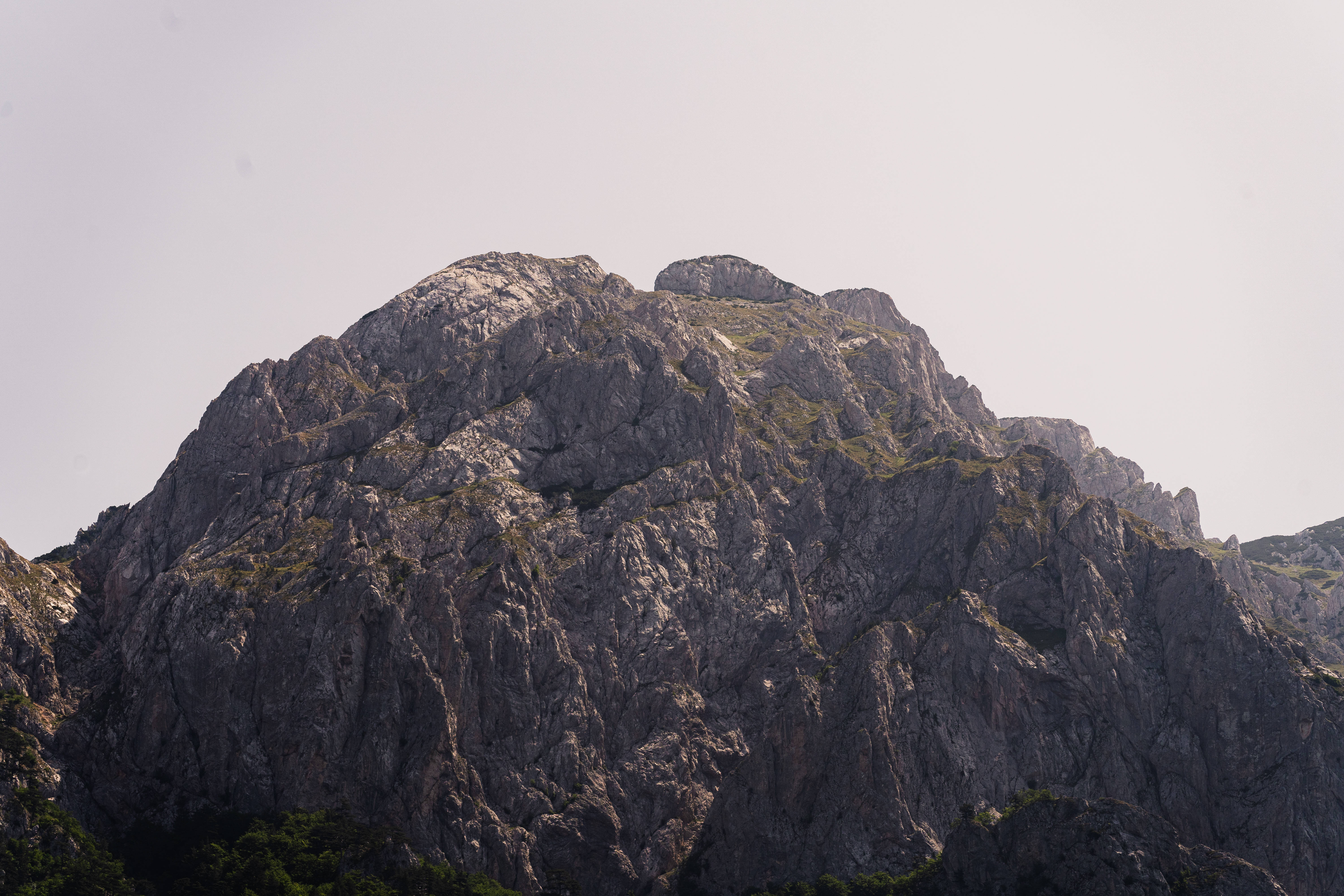 Bosnia And Herzegovina 桌布 壁紙 — 一座崎嶇的灰色山峰，岩石表面參差不齊，稀疏的綠植點綴在蒼白的天空下。