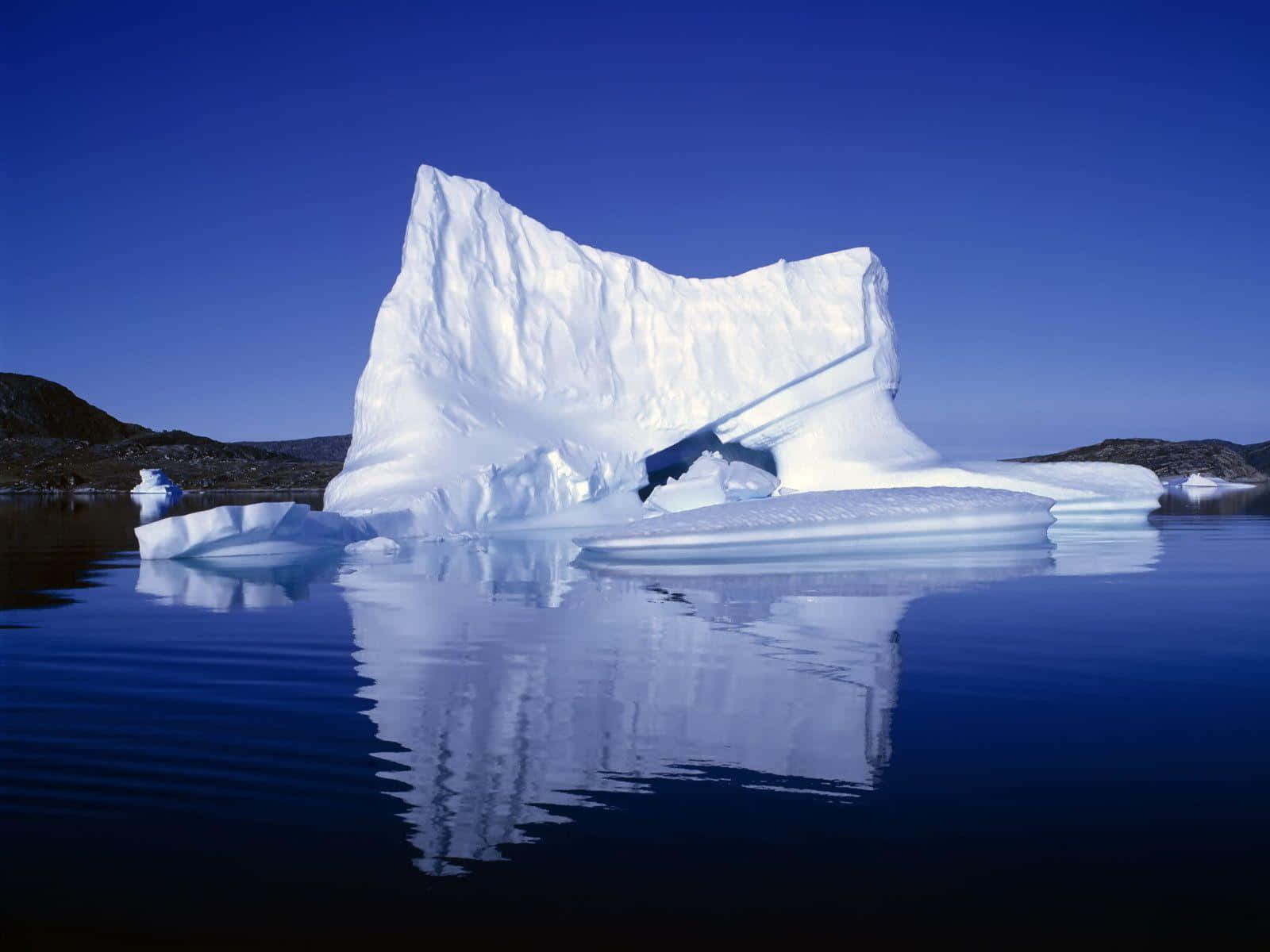 高清 桌布 壁紙 — 一座巨大的冰山，帶有尖銳的山脊和深邃的裂縫，在晴朗的天空下平靜地漂浮在平靜的藍色海水中。