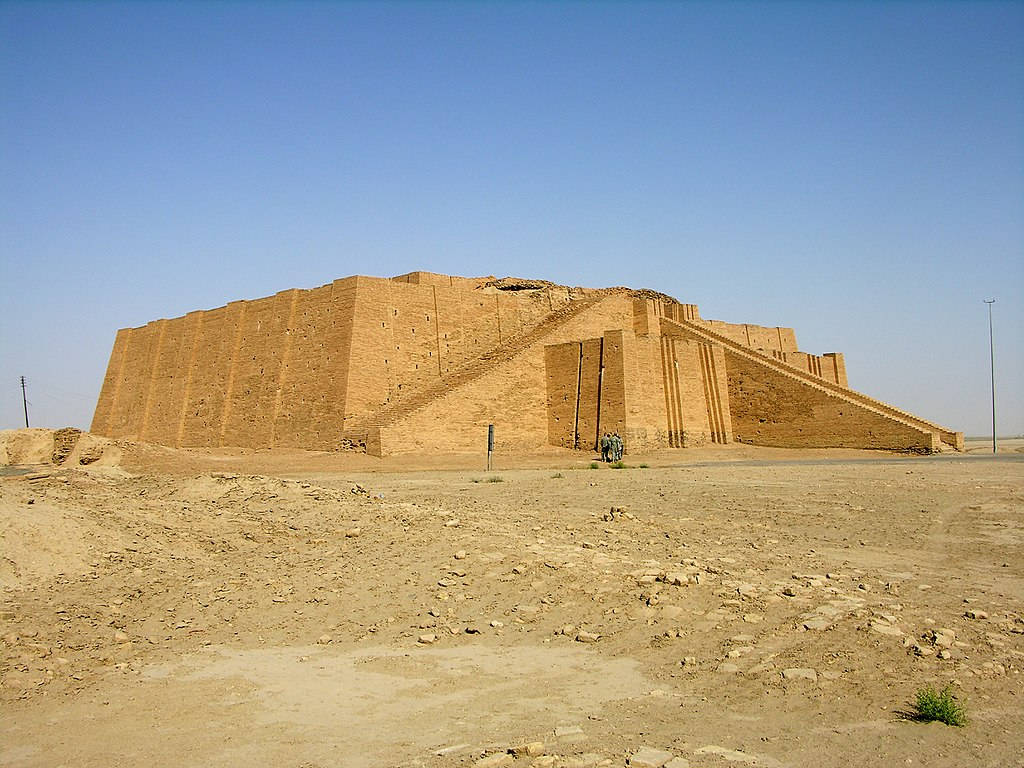 Iraq 桌布 壁紙 — 一座巨大的古代金字形神塔矗立在荒蕪的沙漠中，藍天白雲下，底部有幾位遊客。
