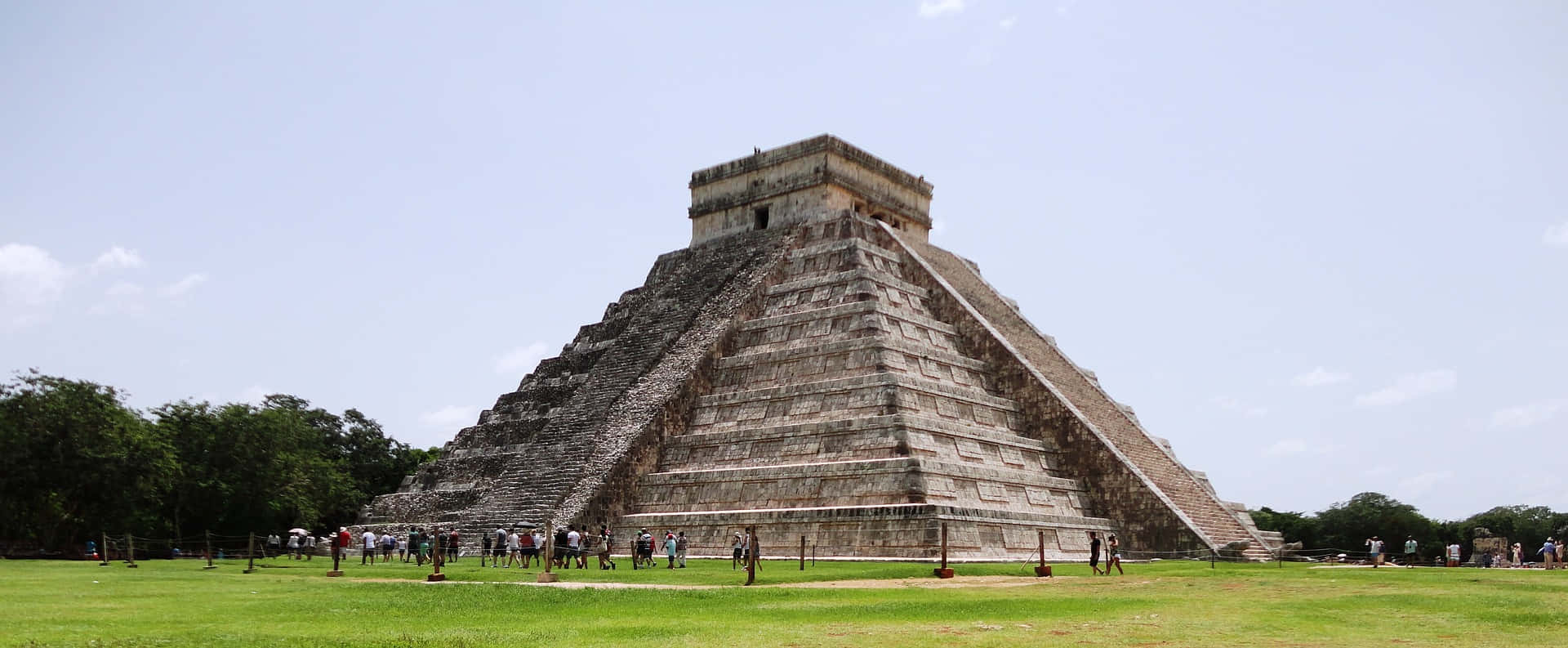 Cancun 桌布 壁紙 — 一座巨大的古瑪雅金字塔從充滿活力的綠色田野中升起，天空湛藍，雲朵點綴。