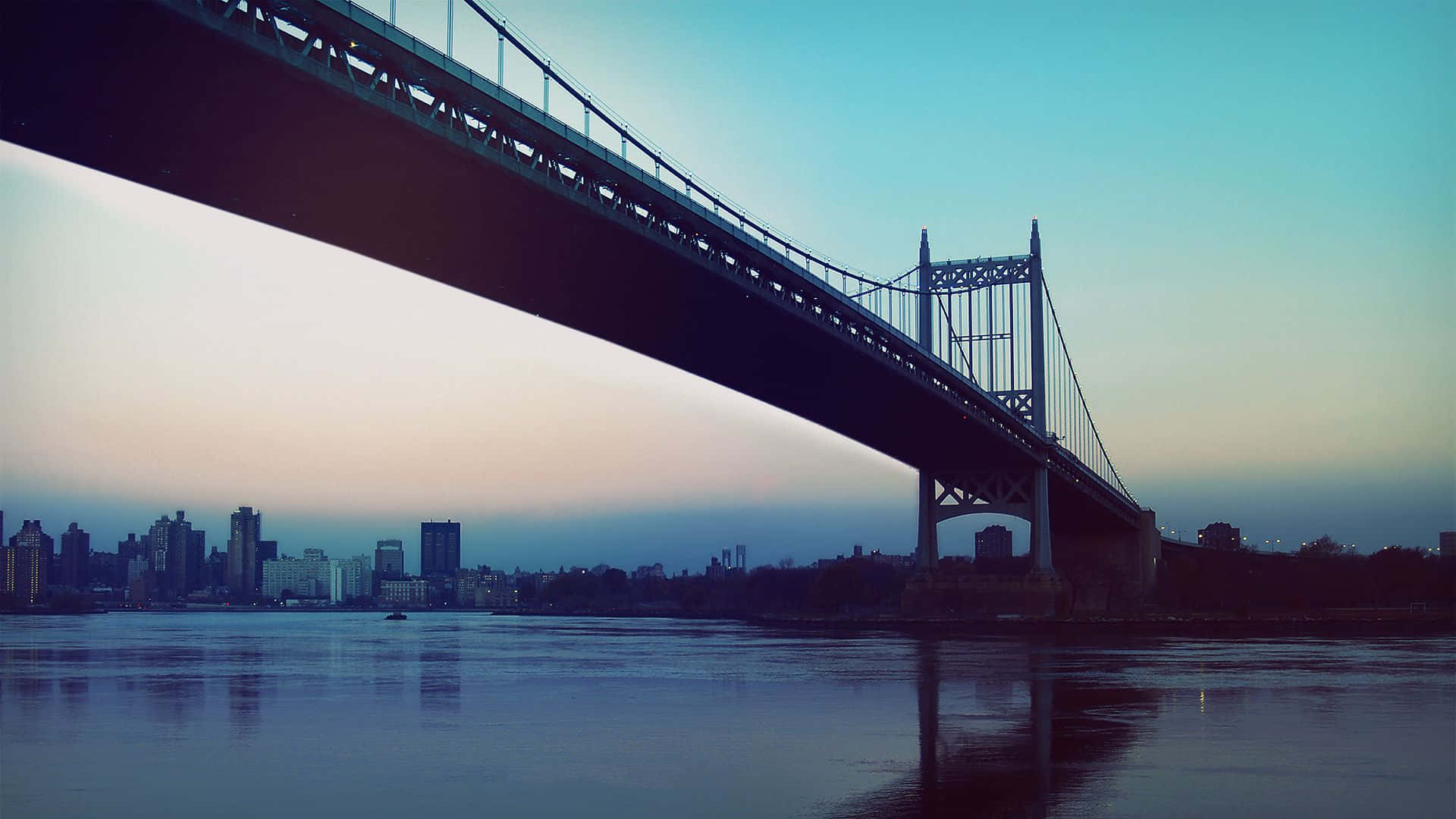 Photography Desktop 桌布 壁紙 — 一座巨大的吊橋在黃昏時分拱起於平靜的河面上，城市天際線倒映在水中。