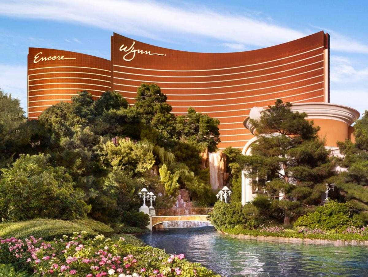 Beautiful Architecture 桌布 壁紙 — 一座巨大的弧形酒店，帶有「Encore」和「Wynn」標誌，在晴朗的藍天下聳立在茂密的綠植和寧靜的水景之上。
