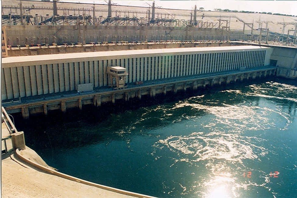 水 桌布 壁紙 — 一座巨大的混凝土水力發電水壩在明亮的日光下將湍急的水流釋放到深藍色的河流中。