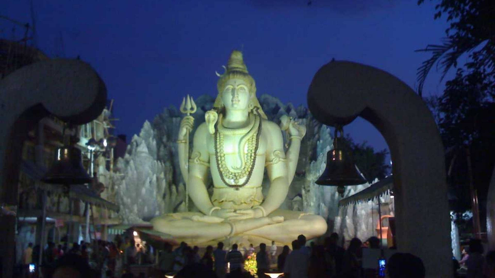 Bangalore 桌布 壁紙 — 一座巨大的發光濕婆神像在黃昏時分靜靜地坐著，信徒們聚集在下方神聖的寺廟庭院中。