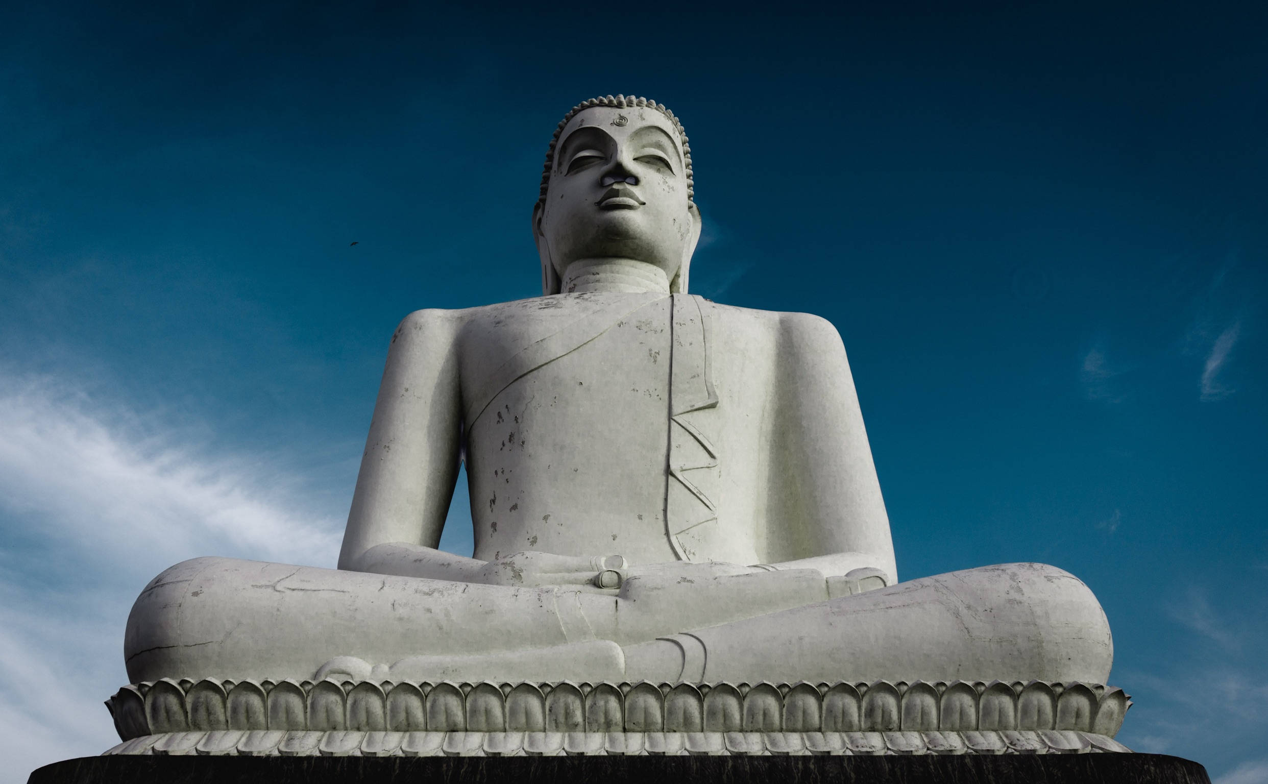 Gautam Buddha 桌布 壁紙 — 一座巨大的白色佛像以蓮花坐姿安詳地坐著，背景是深藍色的天空和縷縷薄雲。
