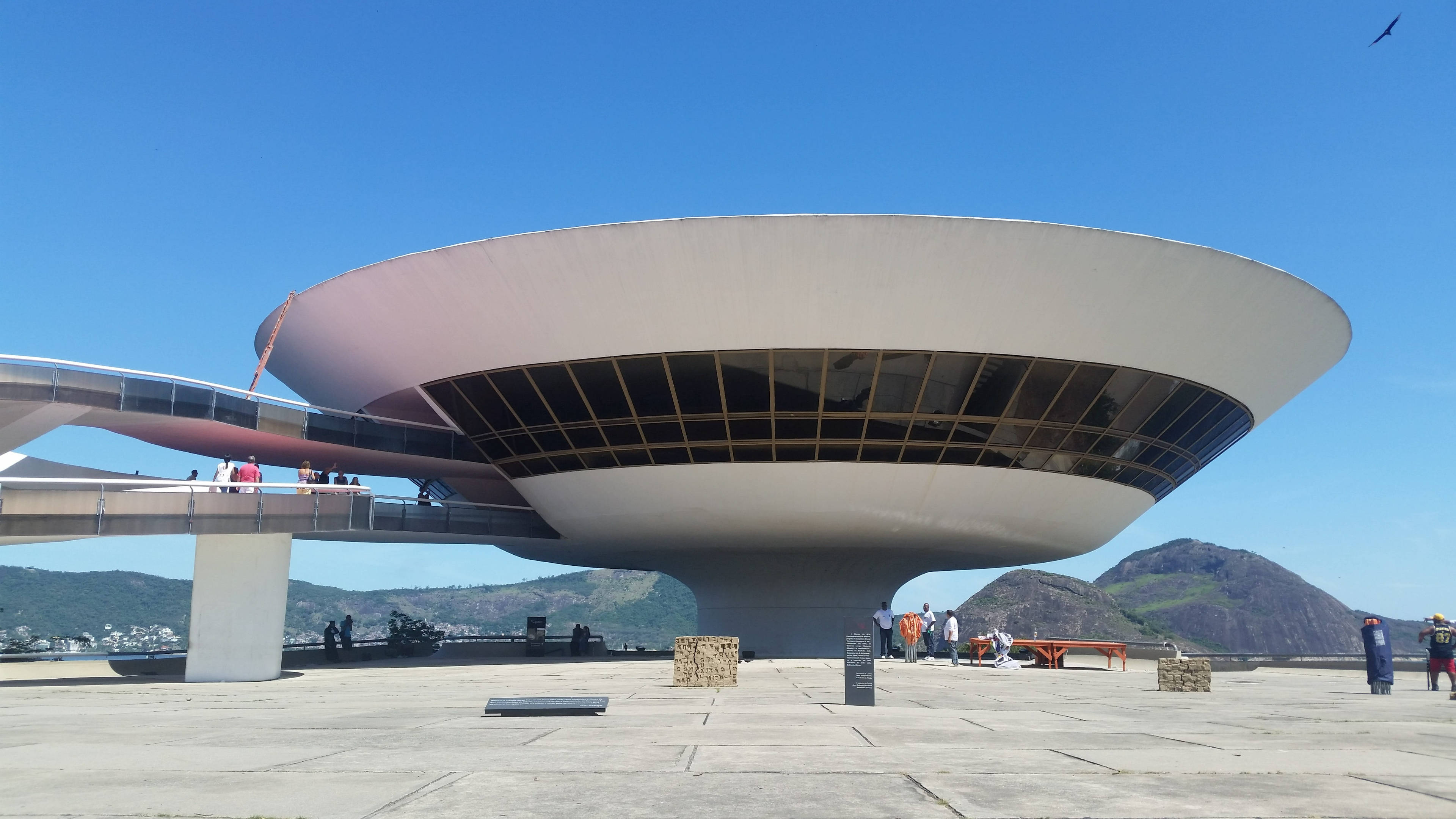 rio 桌布 壁紙 — 一座巨大的白色碟形現代主義建築漂浮在廣場上空，背景是清澈的藍天和遠山。