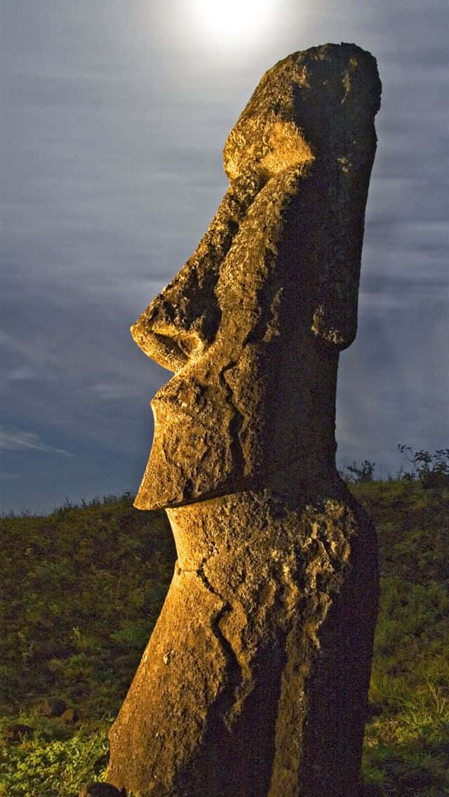 statue 桌布 壁紙 — 一座巨大的石像摩艾雕像在暮色天空下剪影而立，上方有一輪明亮的月亮。