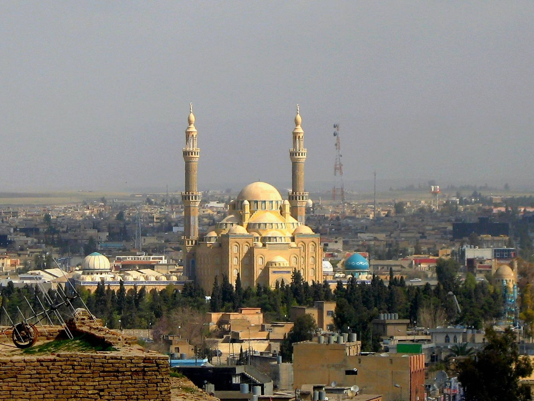 Iraq 桌布 壁紙 — 一座巨大的米色清真寺，擁有雙宣禮塔，在朦朧的天空下，聳立在廣闊的城市景觀之上。