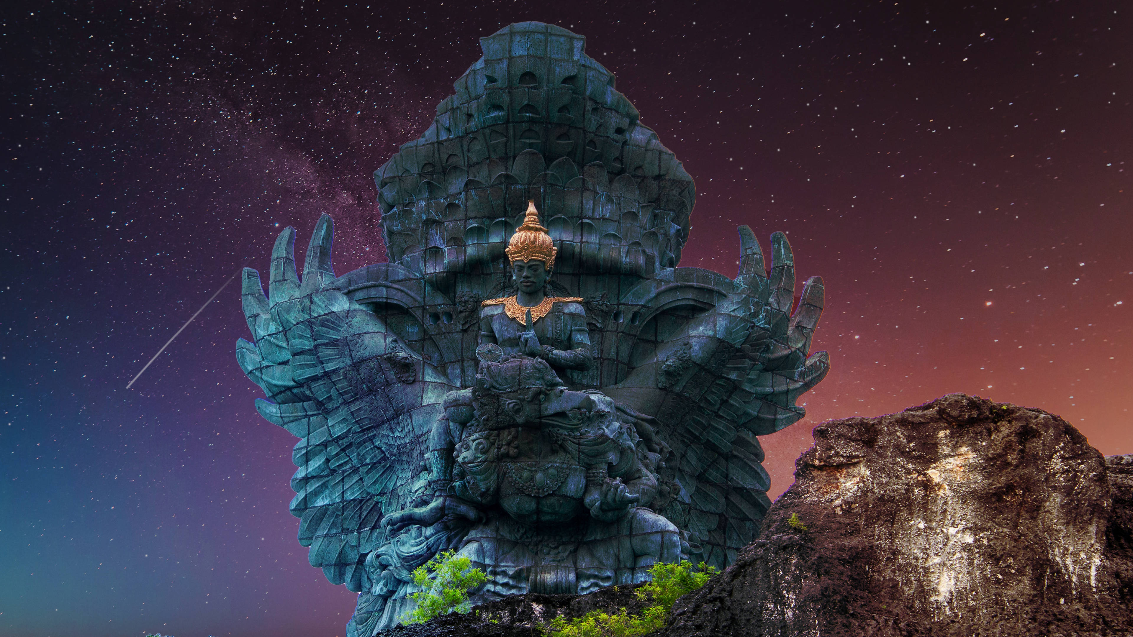 Vishnu 桌布 壁紙 — 一座巨大的青綠色多臂神祇雕像，頭戴金色皇冠，矗立在岩石露頭上，背景是星光燦爛的黃昏天空，有一顆流星劃過。