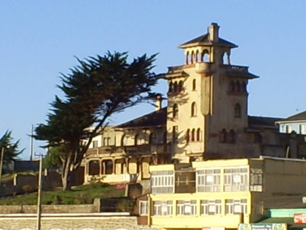 Chile 桌布 壁紙 — 一座帶有塔樓的大型歷史建築矗立在黃色建築旁邊，附近有一棵大樹，天空清澈湛藍。