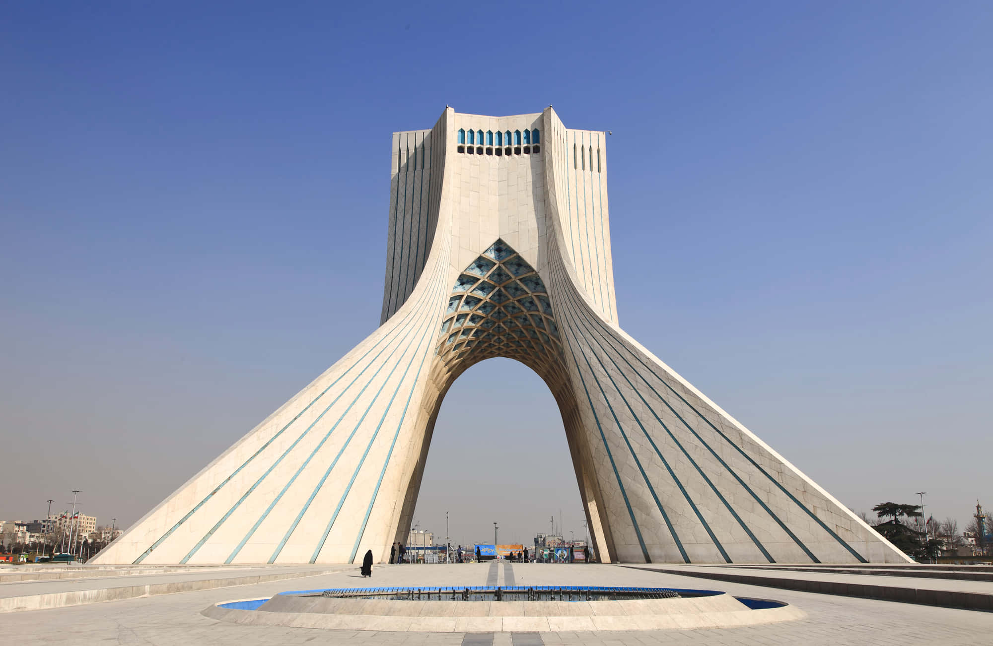 Tehran 桌布 壁紙 — 一座帶有幾何圖案的白色拱門紀念碑在晴朗的藍天下高聳，一個小人影在反射池附近行走。