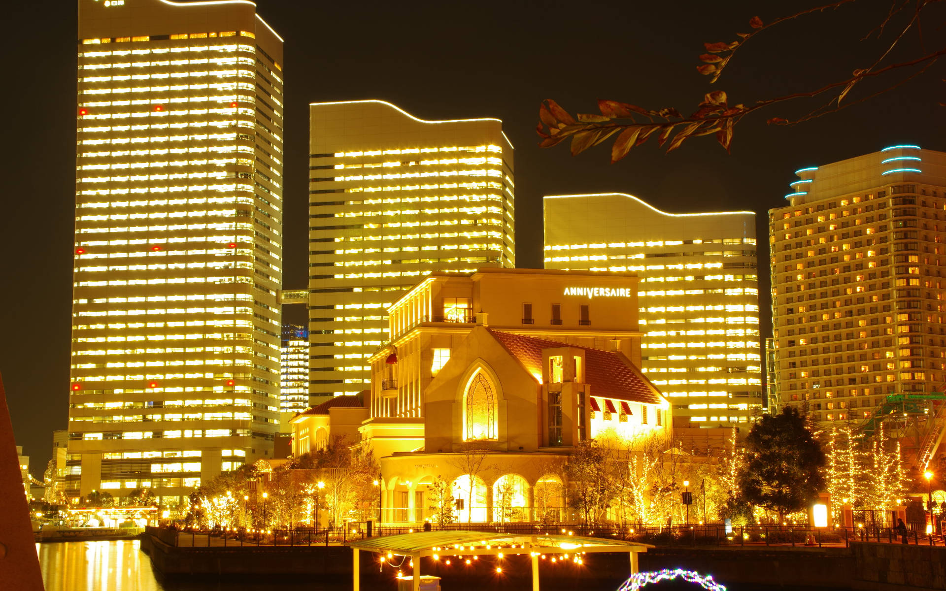 Yokohama 桌布 壁紙 — 一座帶有溫暖燈光的歐式建築在夜晚矗立於河邊，被高聳的燈光摩天大樓所環繞。