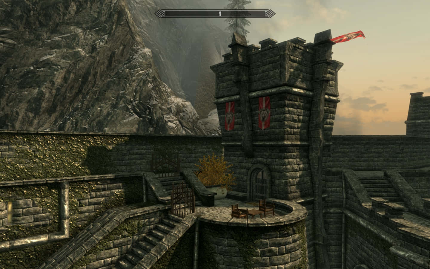 Skyrim Solitude 桌布 壁紙 — 一座帶有紅色旗幟的石城堡塔樓矗立在懸崖頂上，俯瞰著日落時分霧氣瀰漫的山谷。