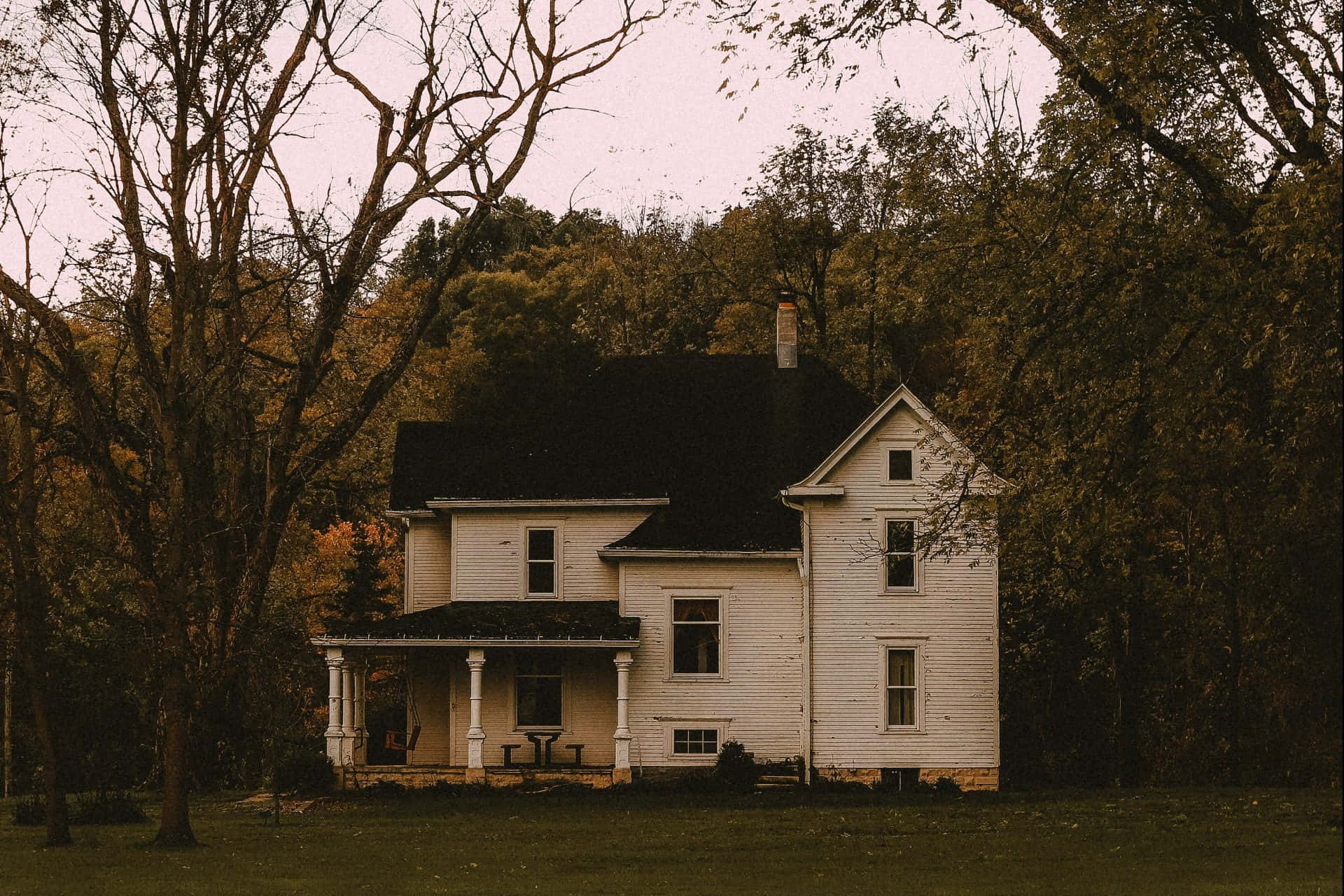 Haunted House 桌布 壁紙 — 一座帶門廊的風化白色農舍，獨自矗立在濃密的秋日森林中，天空暗淡。