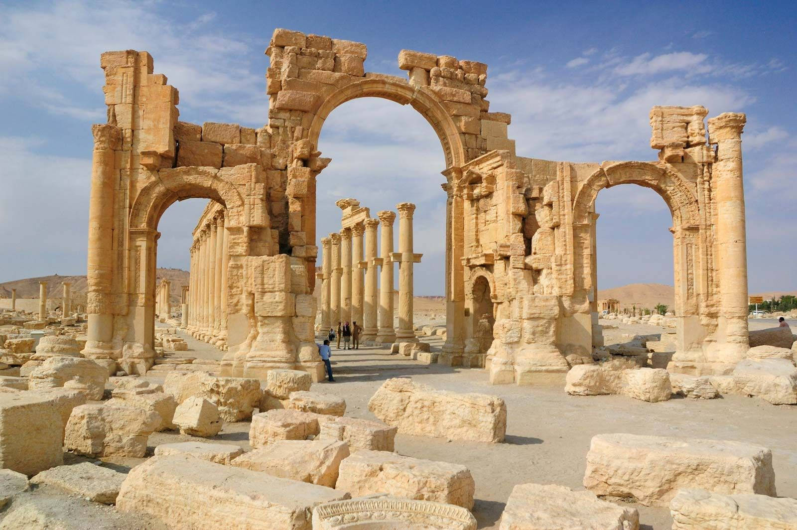Syria 桌布 壁紙 — 一座廢墟神廟的古老石拱門和柱子，在沙漠景觀中，在明亮的藍天下高高聳立。