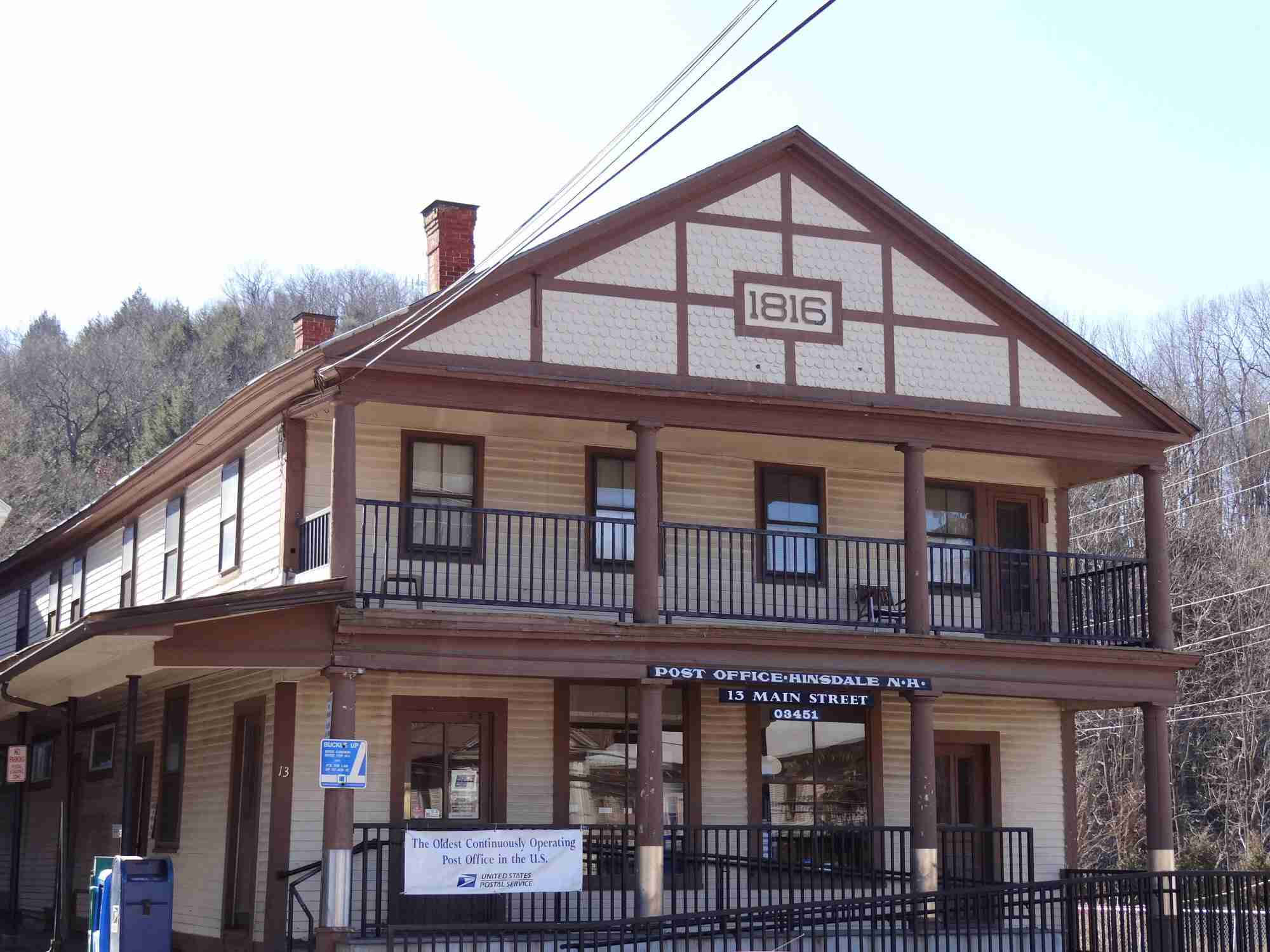 Post Office 桌布 壁紙 — 一座建於1816年的歷史郵局建築，擁有木質牆板和陽台，矗立在晴朗的天空下，背景是光禿禿的樹木。