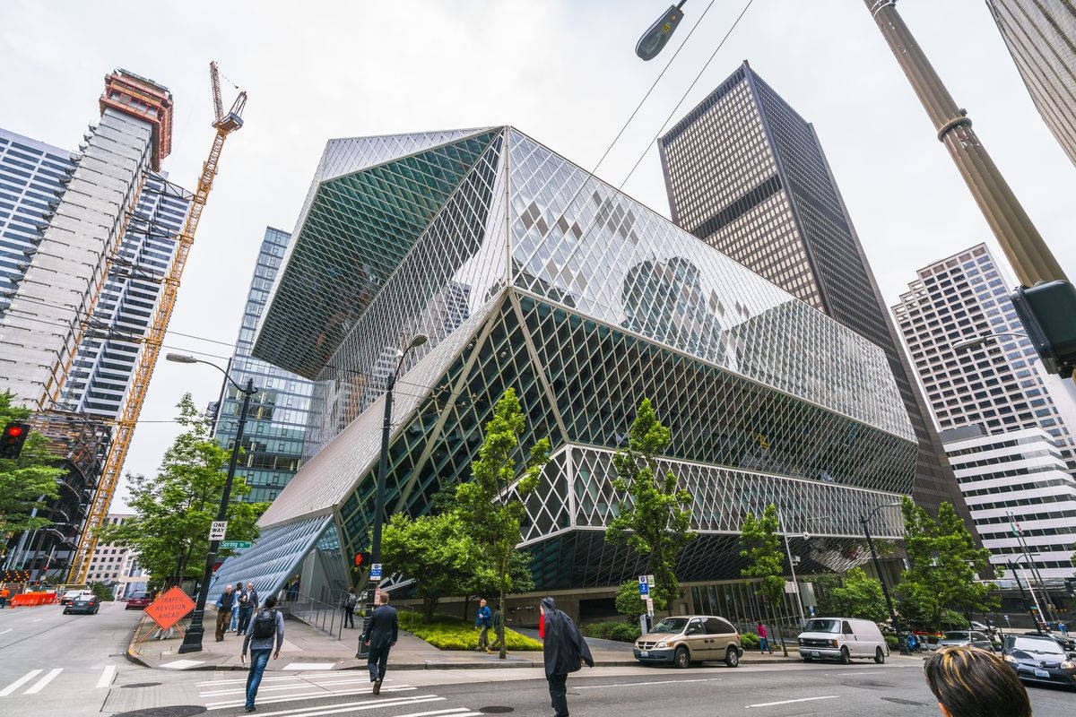 Library 桌布 壁紙 — 一座引人注目的幾何玻璃建築，鑽石圖案外牆，聳立在繁華的城市景觀中，周圍環繞著摩天大樓和行人。