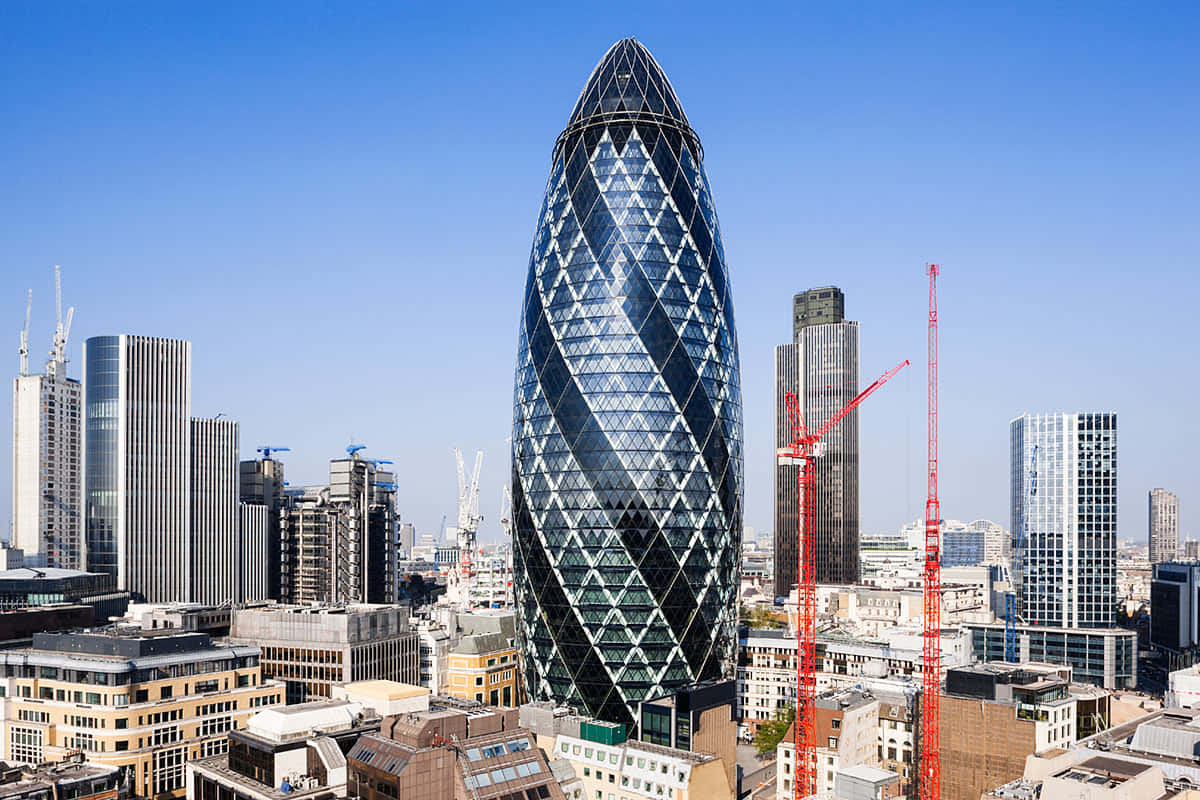Skyscraper 桌布 壁紙 — 一座引人注目的玻璃摩天大樓，帶有扭曲的鑽石圖案，在密集的城市天際線和建築起重機上方，主宰著明亮的藍天。