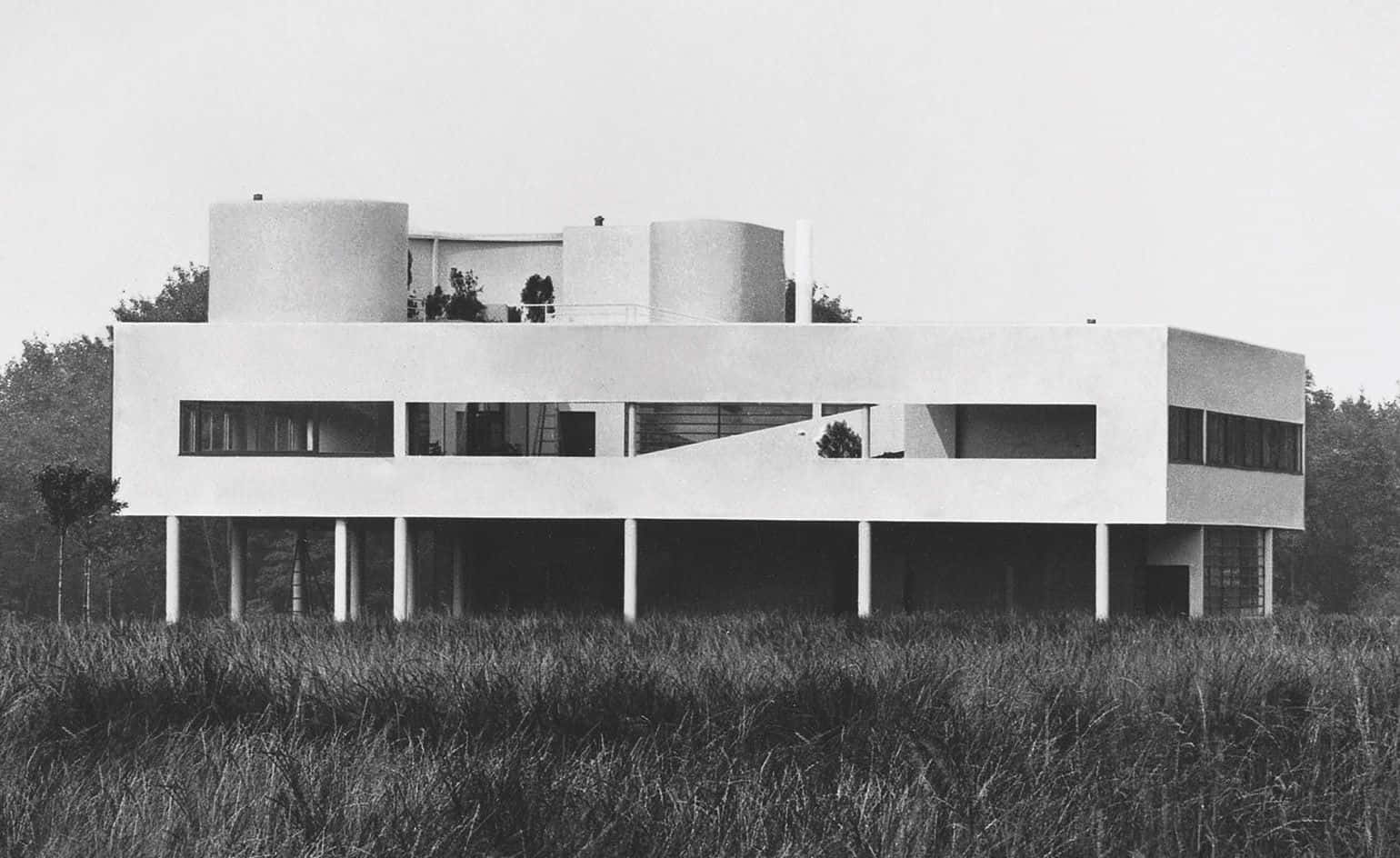 Black And White Architecture 桌布 壁紙 — 一座引人注目的現代主義房屋，擁有圓柱形塔樓和懸臂式陽台，孤立地矗立在陰天下的高草田野中。