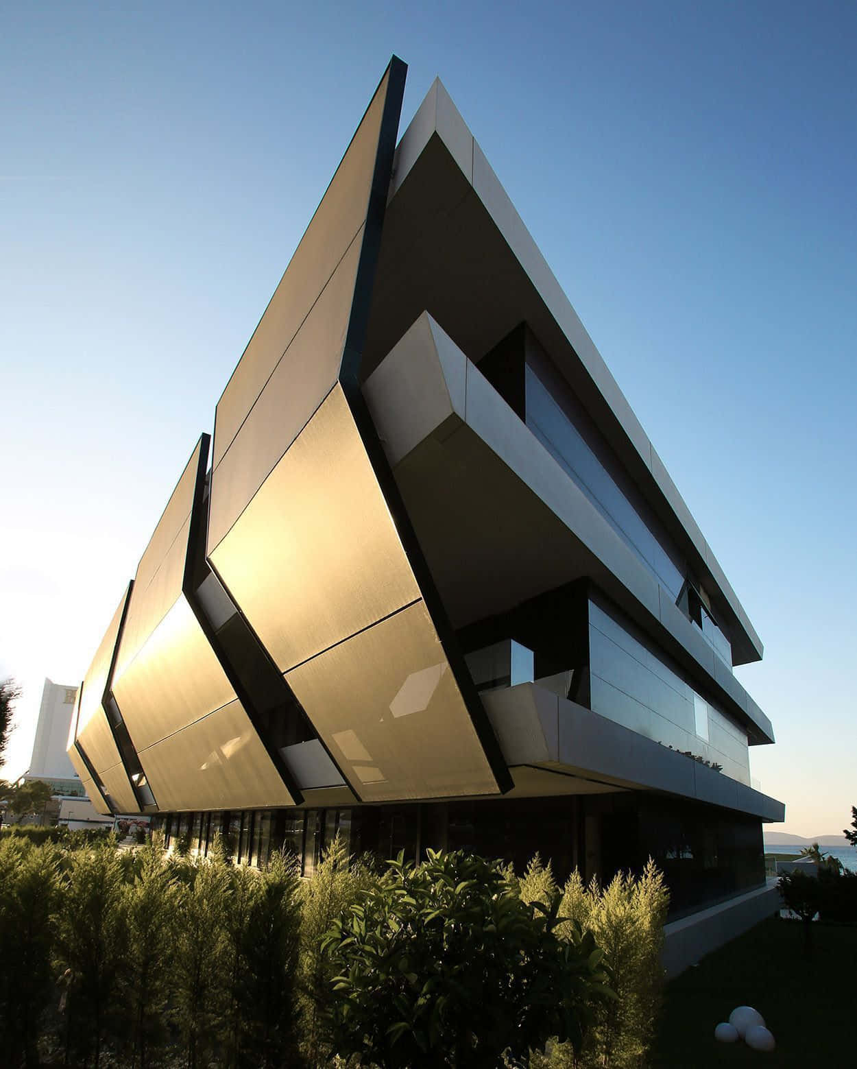 Minimalist Architecture 桌布 壁紙 — 一座引人注目的現代建築，擁有幾何金色和玻璃外牆，在晴朗的藍天下沐浴在金色陽光中。