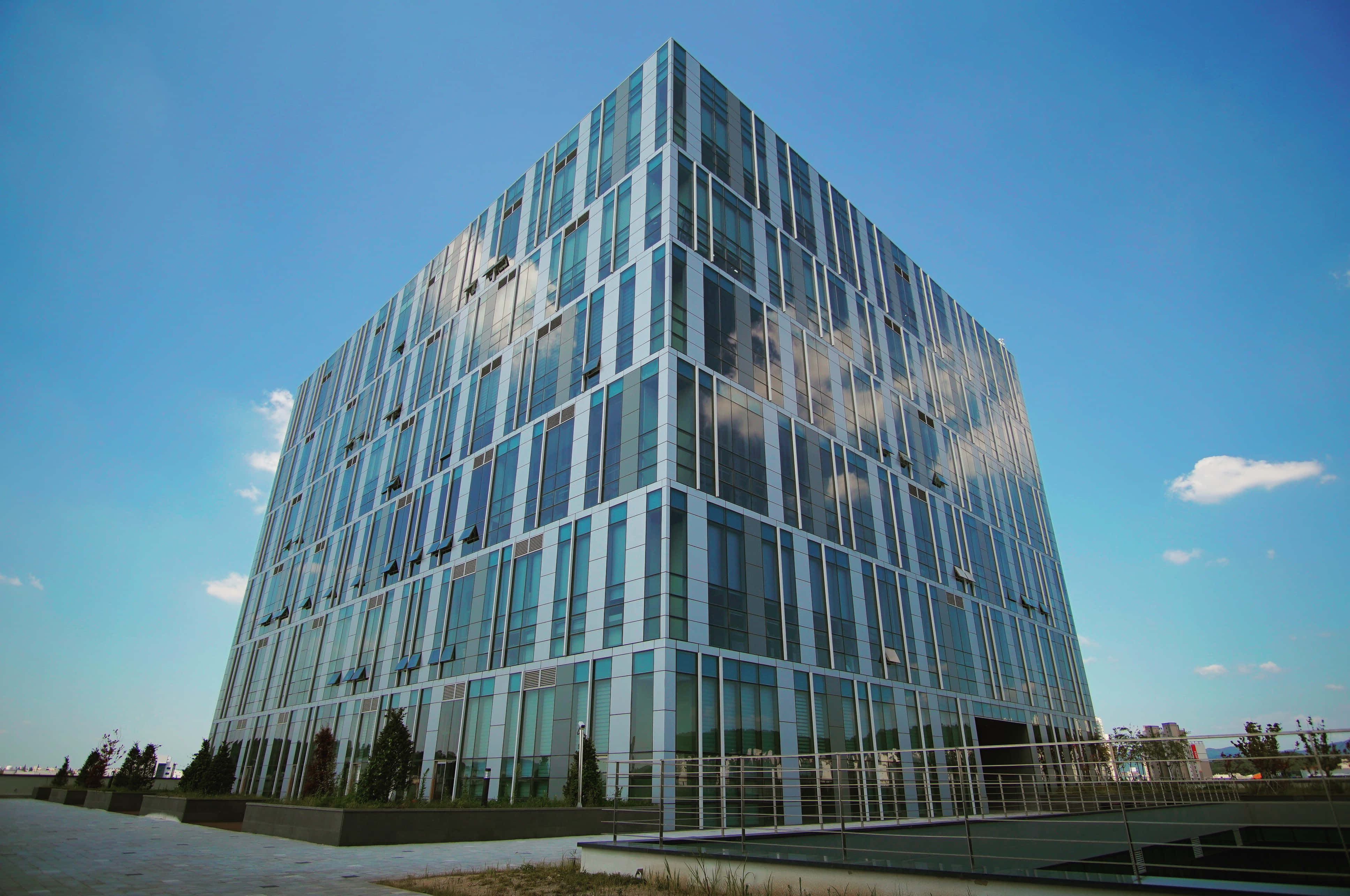 Building 桌布 壁紙 — 一座引人注目的現代玻璃摩天大樓在明亮的白天背景下反射出清澈的藍天和散落的雲朵。