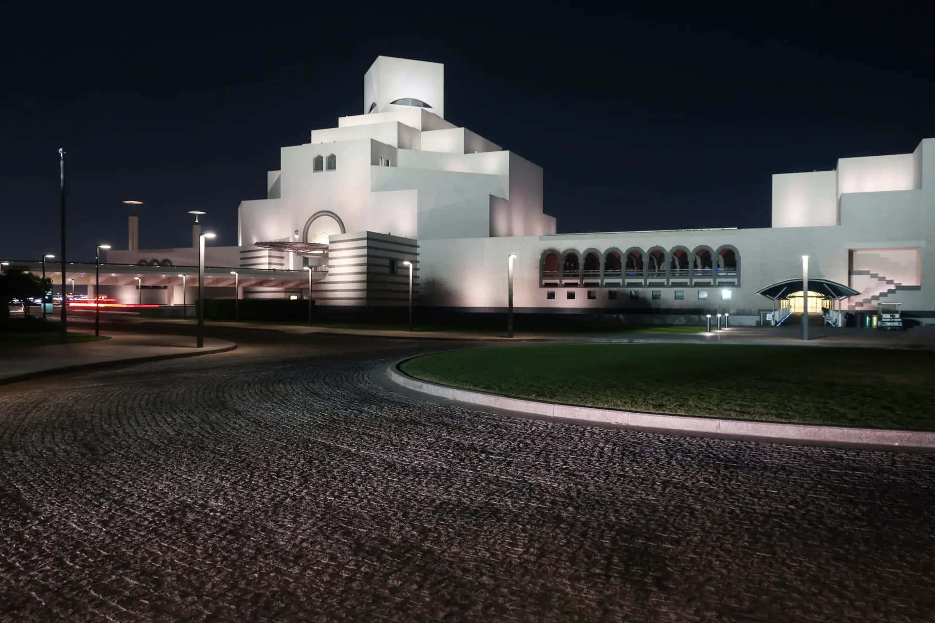 Museum Of Islamic Art 桌布 壁紙 — 一座引人注目的現代白色建築在夜間被溫暖的燈光照亮，映襯著黑暗的天空和前景的鵝卵石車道。