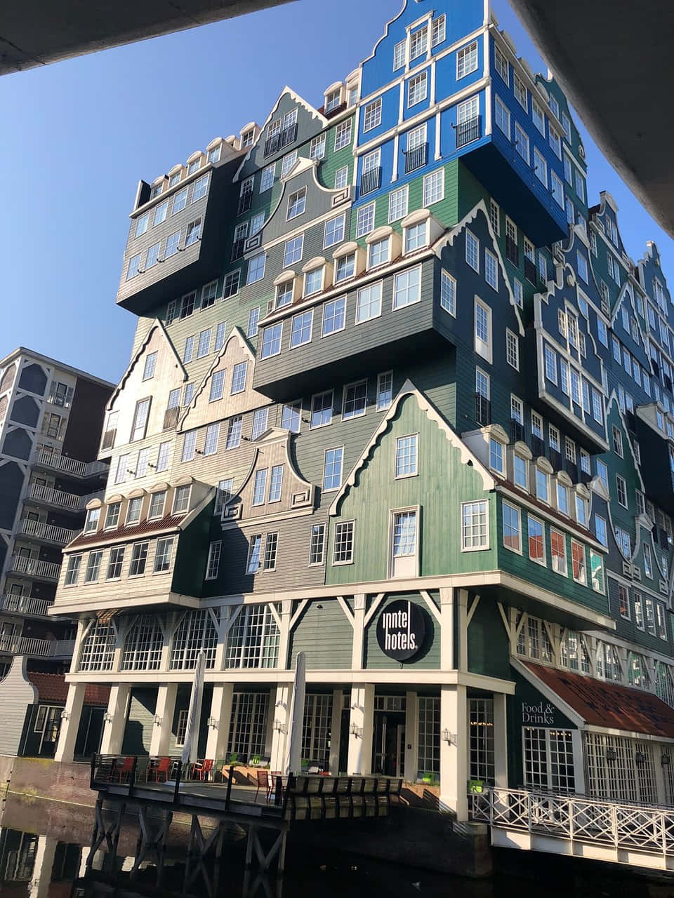 建築 桌布 壁紙 — 一座引人注目的現代酒店建築，在清澈的藍天下，擁有堆疊的荷蘭式山牆立面，顏色為綠色、藍色和灰色。