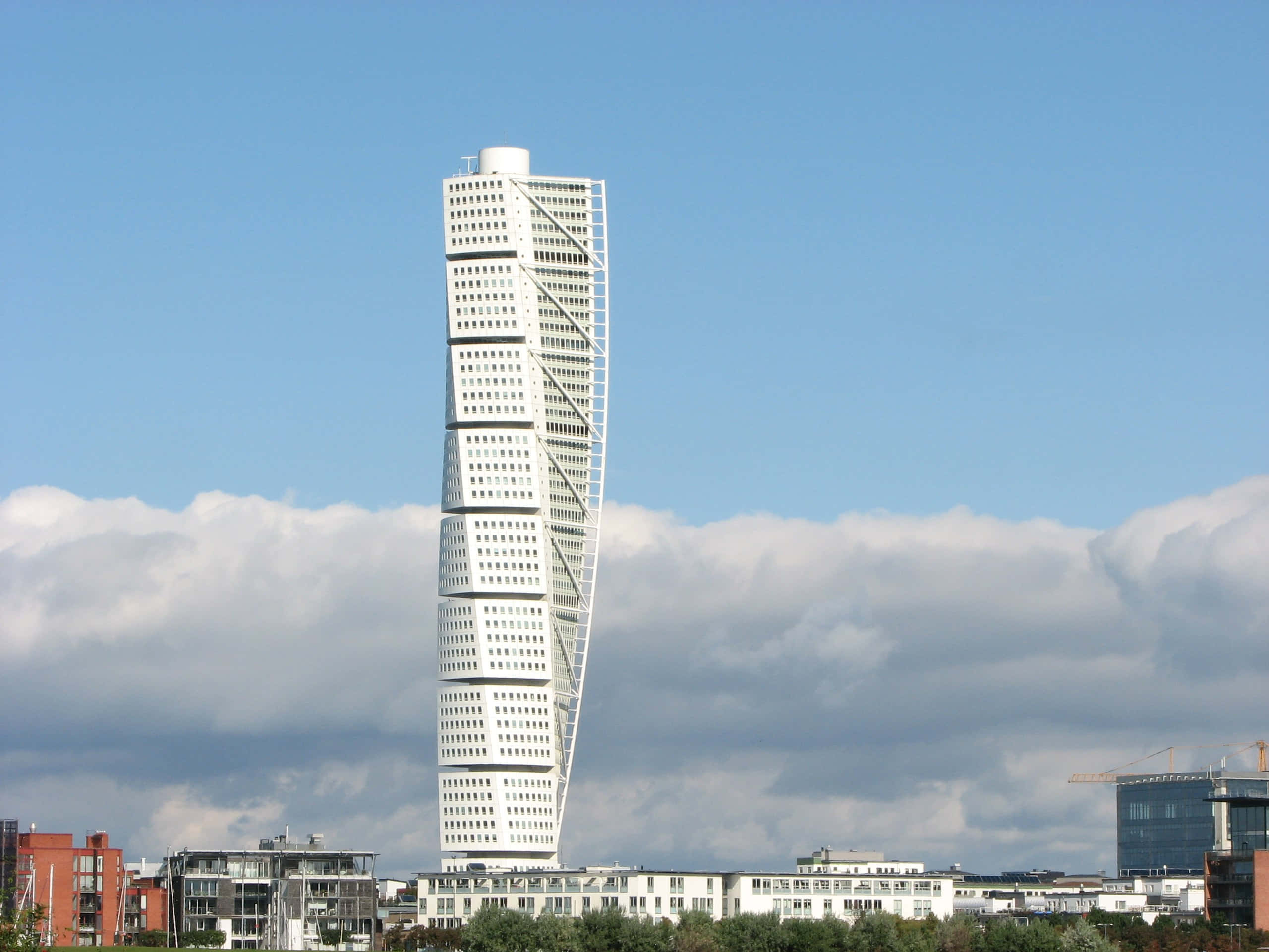 Skyscraper 桌布 壁紙 — 一座引人注目的白色扭曲摩天大樓在部分多雲的藍天下，聳立於現代城市天際線之上。