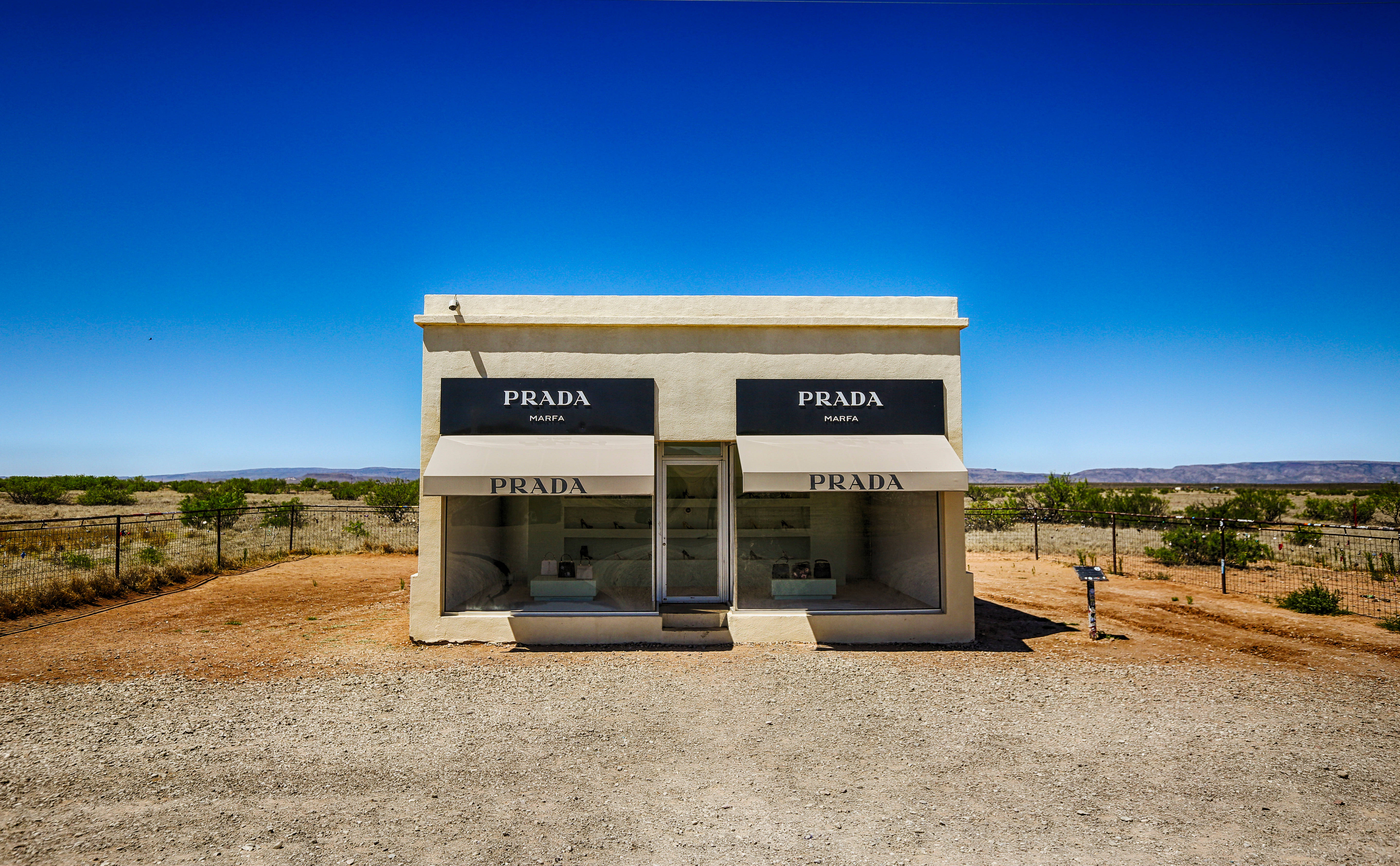德州 桌布 壁紙 — 一座引人注目的米色 Prada Marfa 店面獨自矗立在廣闊乾旱的沙漠中，天空清澈湛藍。