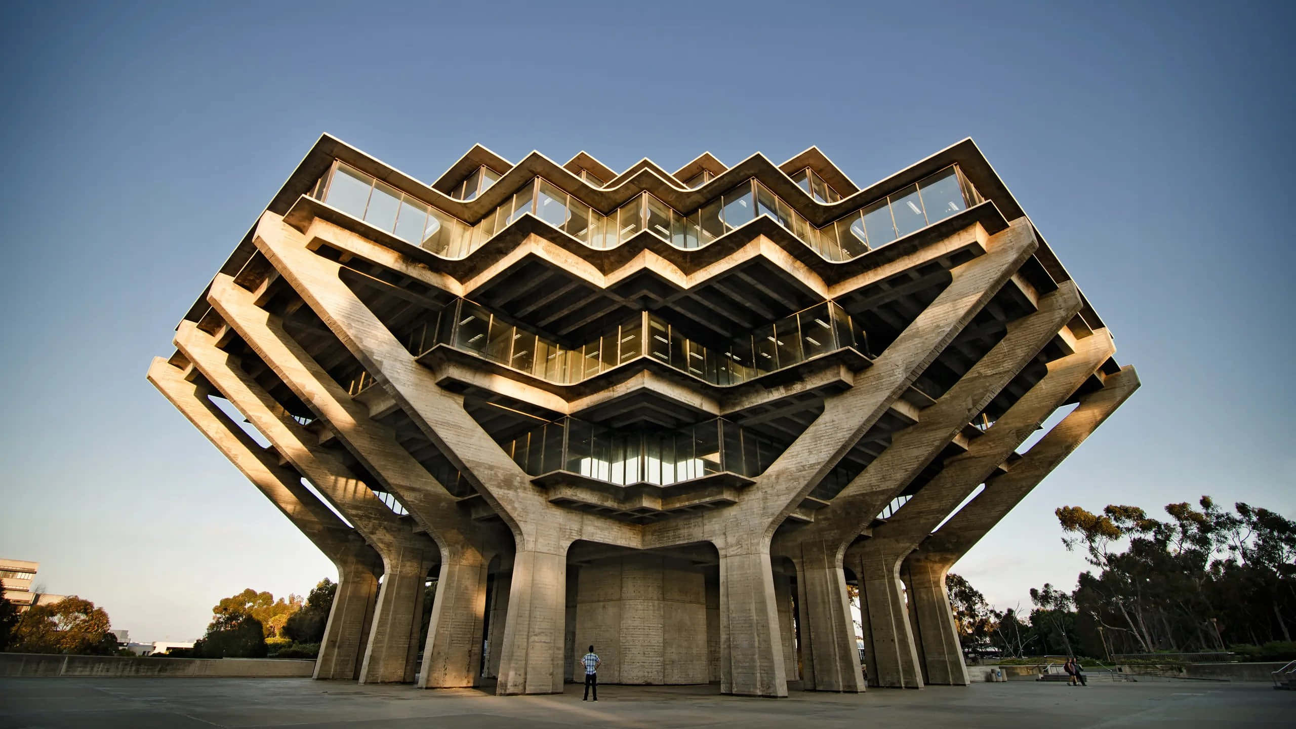Building 桌布 壁紙 — 一座引人注目的粗獷主義混凝土建築，帶有鋸齒狀玻璃陽台，在黃昏時分聳立在清澈的藍天下。