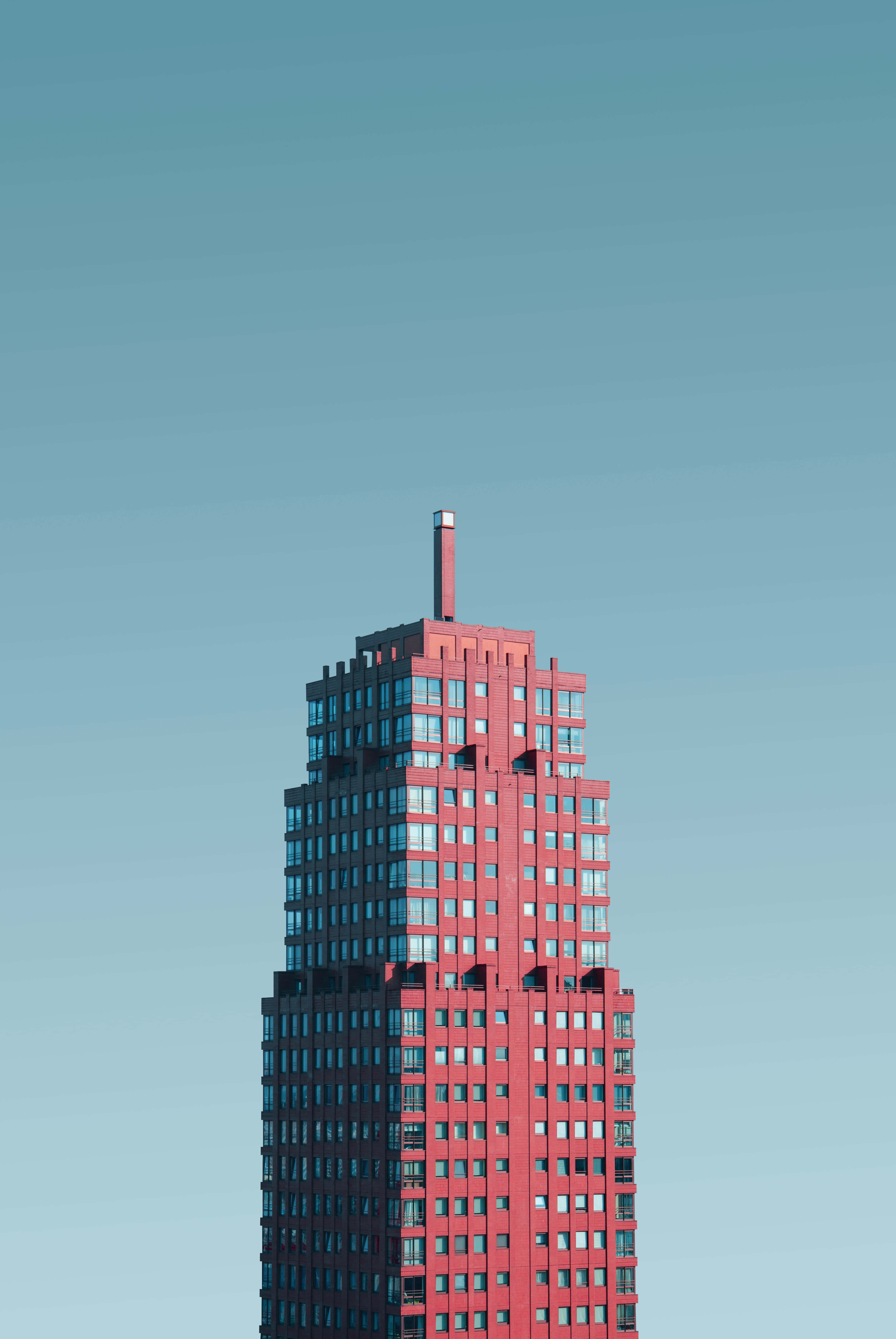 Building 桌布 壁紙 — 一座引人注目的紅色現代摩天大樓以極簡構圖在清澈的藍天下聳立。