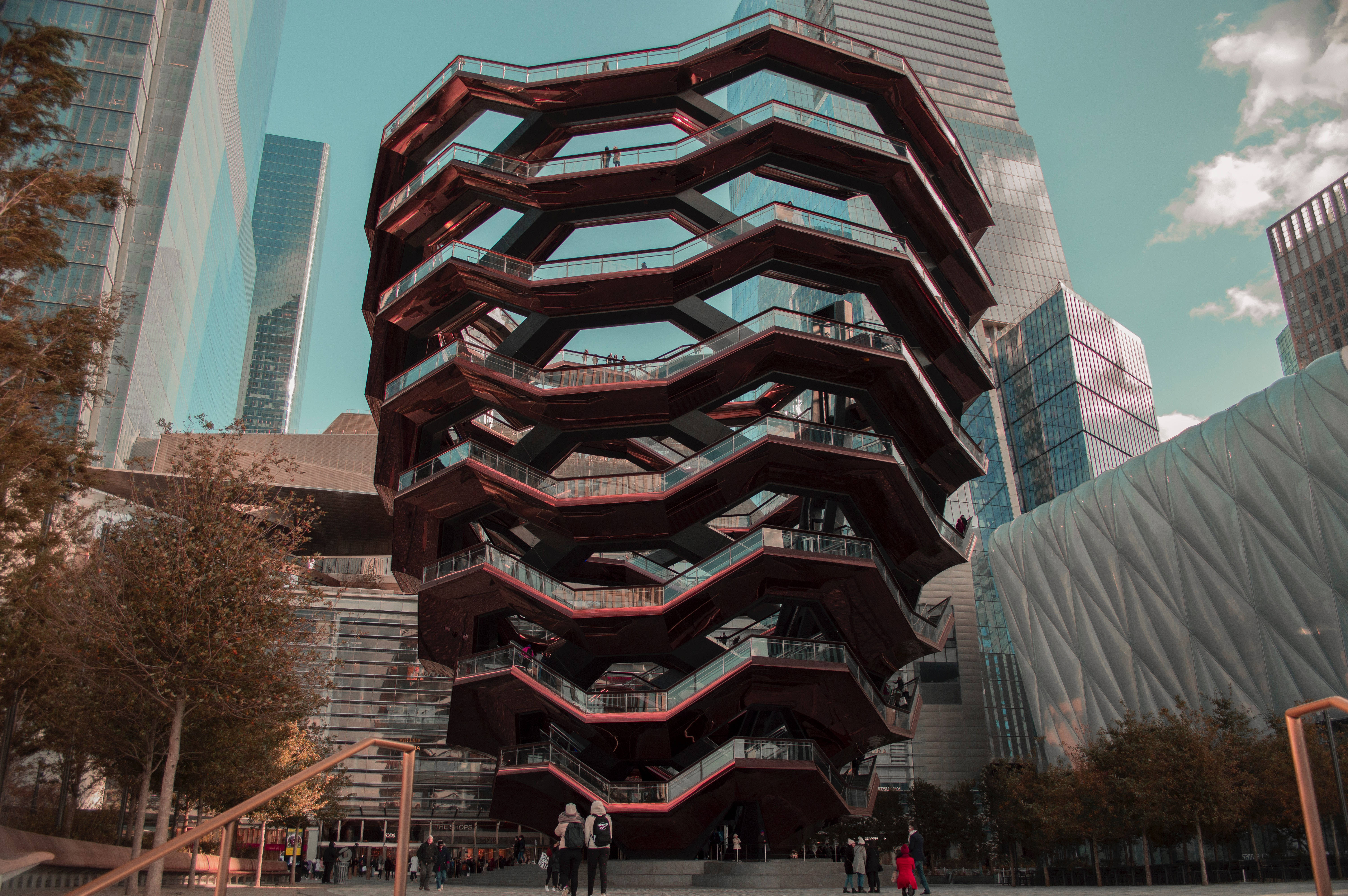 Nyc Aesthetic 桌布 壁紙 — 一座引人注目的紅色蜂窩狀建築結構，配有玻璃欄杆，在晴朗的藍天下聳立於現代摩天大樓之間。