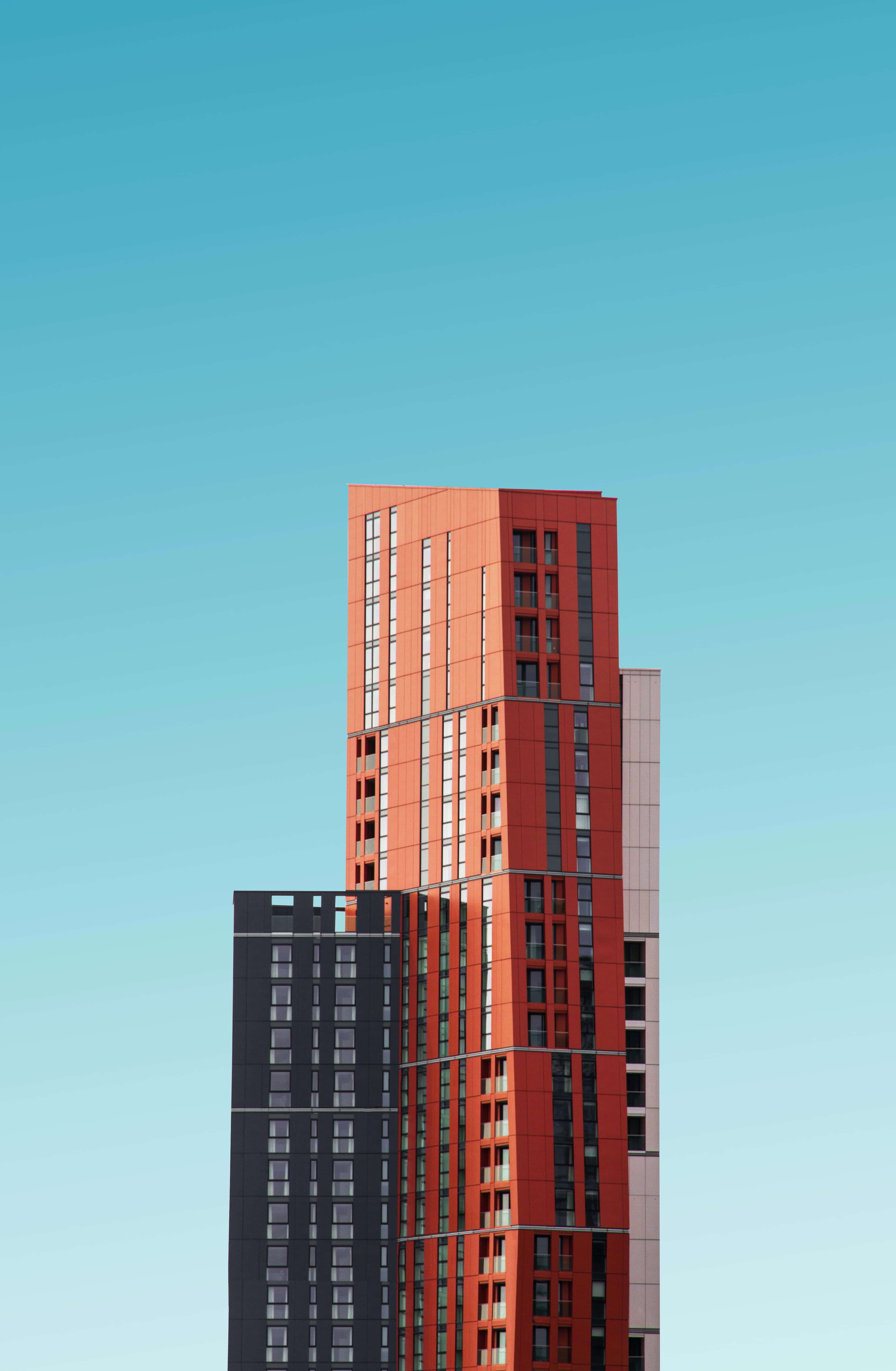 Building 桌布 壁紙 — 一座引人注目的紅黑摩天大樓以乾淨的幾何線條和重複的窗戶圖案刺穿清澈的藍天。